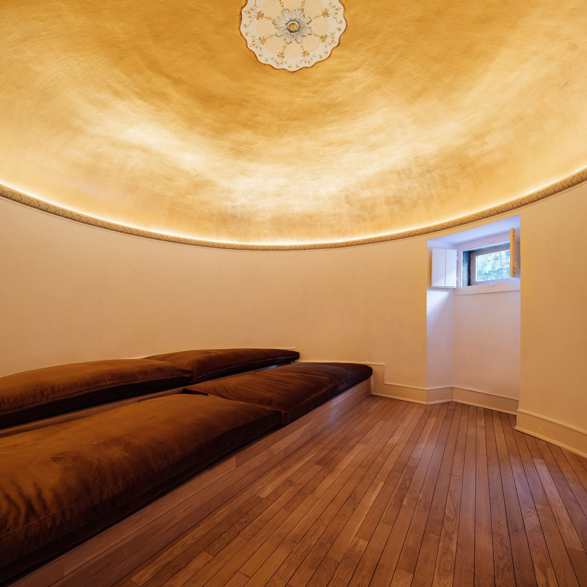 Circular bedroom with domed gilded ceiling, indirect lighting at the cornice, and small high window