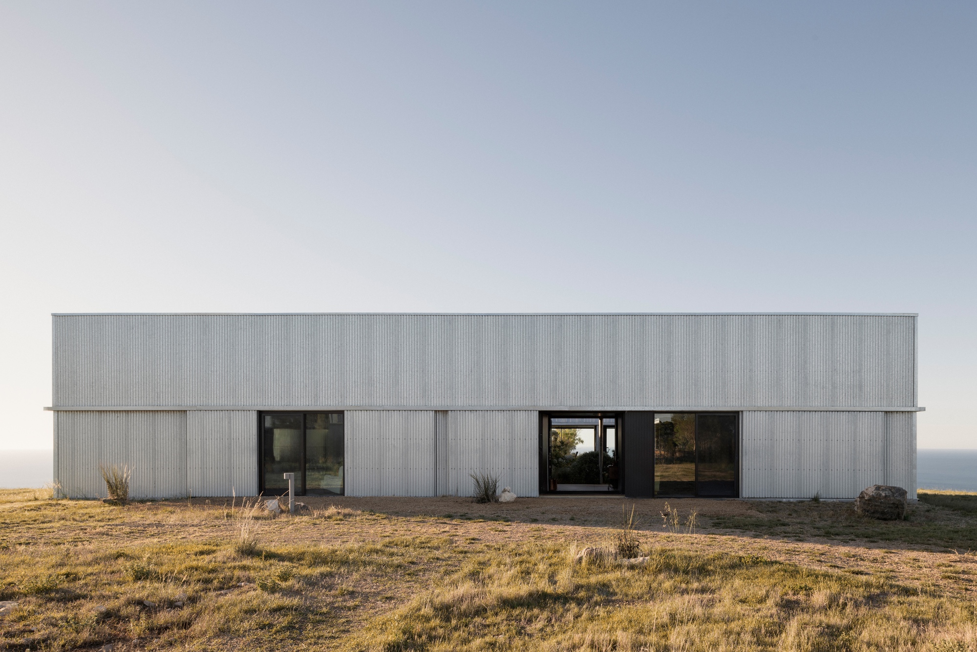 Corrugated metal facade with multiple openings overlooking dry grassland and horizon