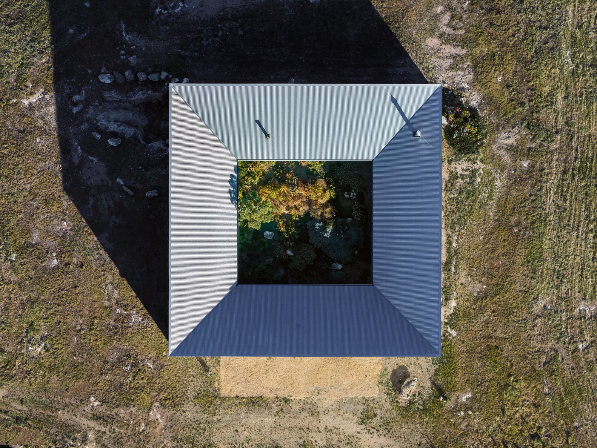 Aerial view of square courtyard plan with central tree and corrugated metal roof