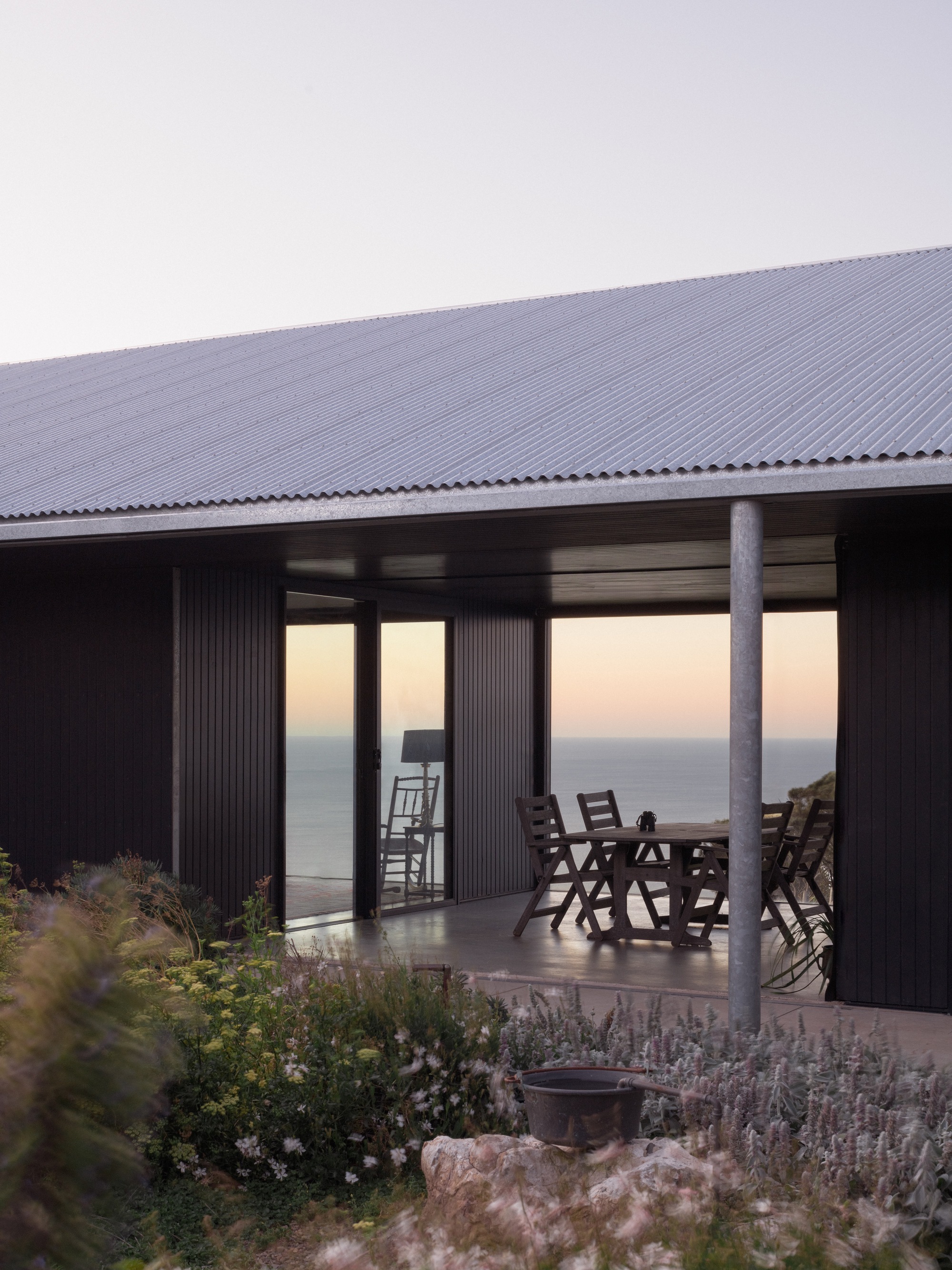Covered terrace with steel columns and outdoor furniture facing the ocean at twilight