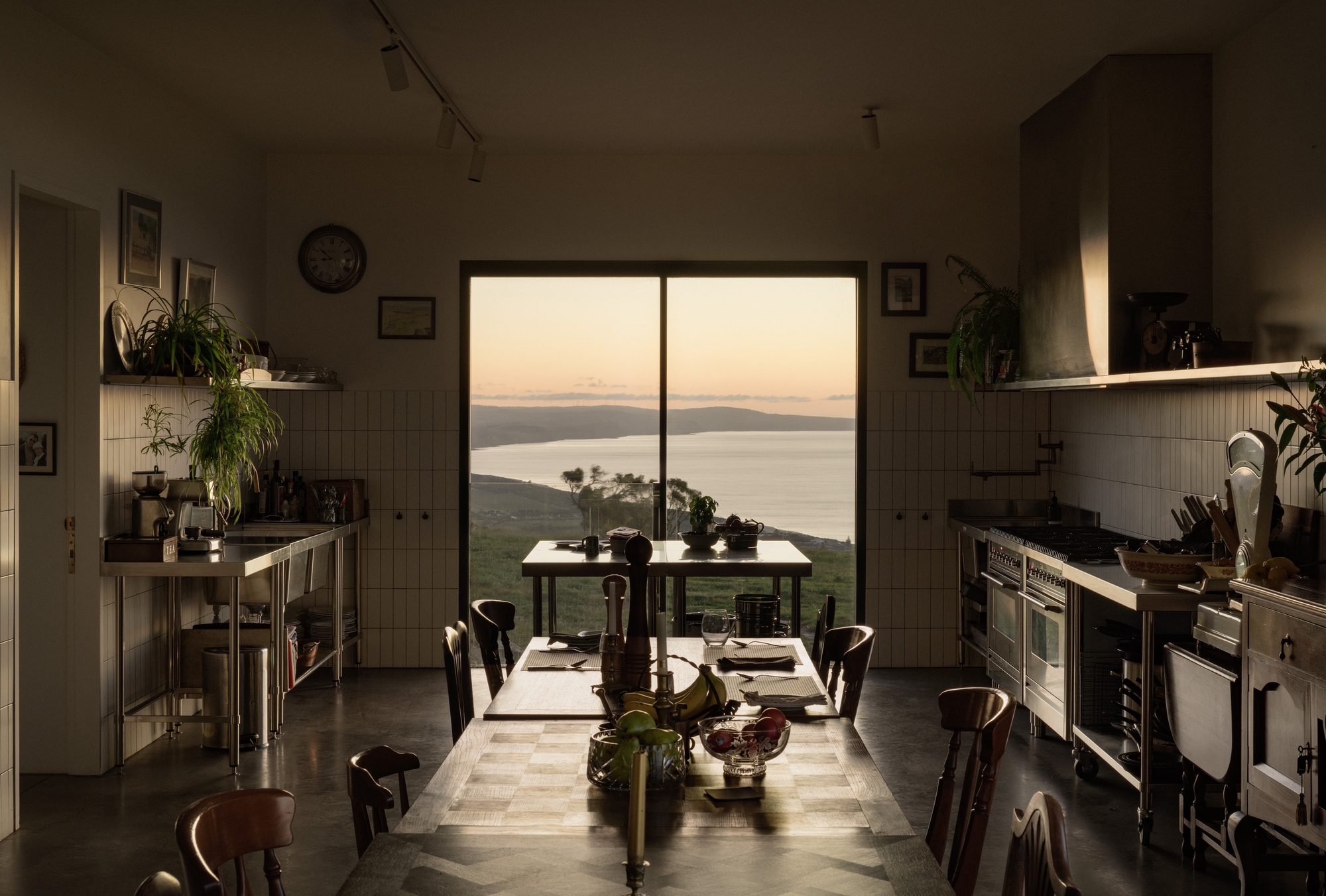 Kitchen with central dining table framing a window view to the sea at dusk