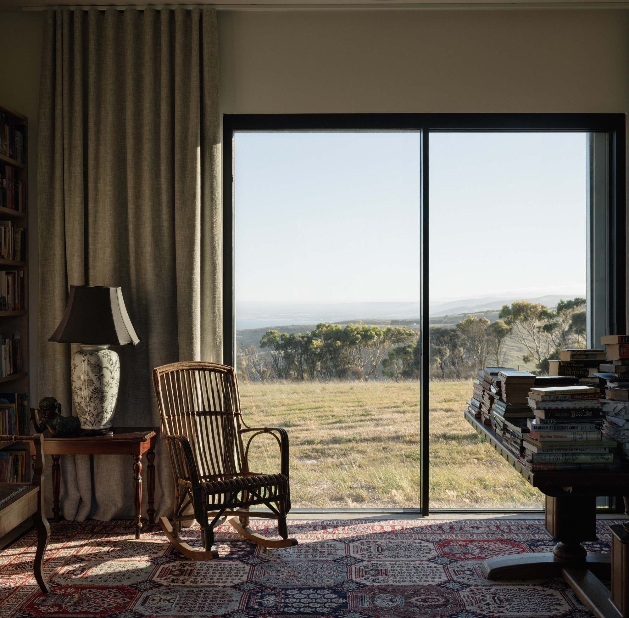 Floor-to-ceiling window framing a view of grassland and distant trees with a rocking chair on a patterned rug
