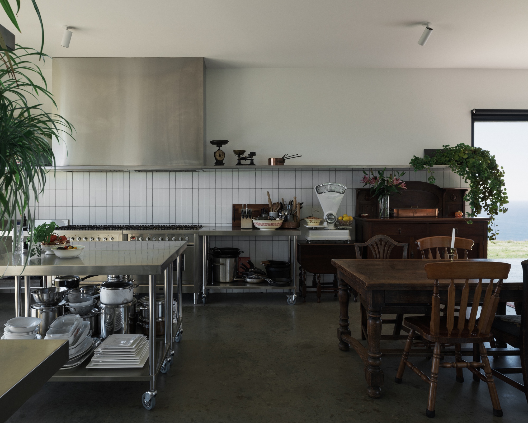 Open kitchen with white subway tile backsplash, stainless steel range hood, and timber dining table with view beyond