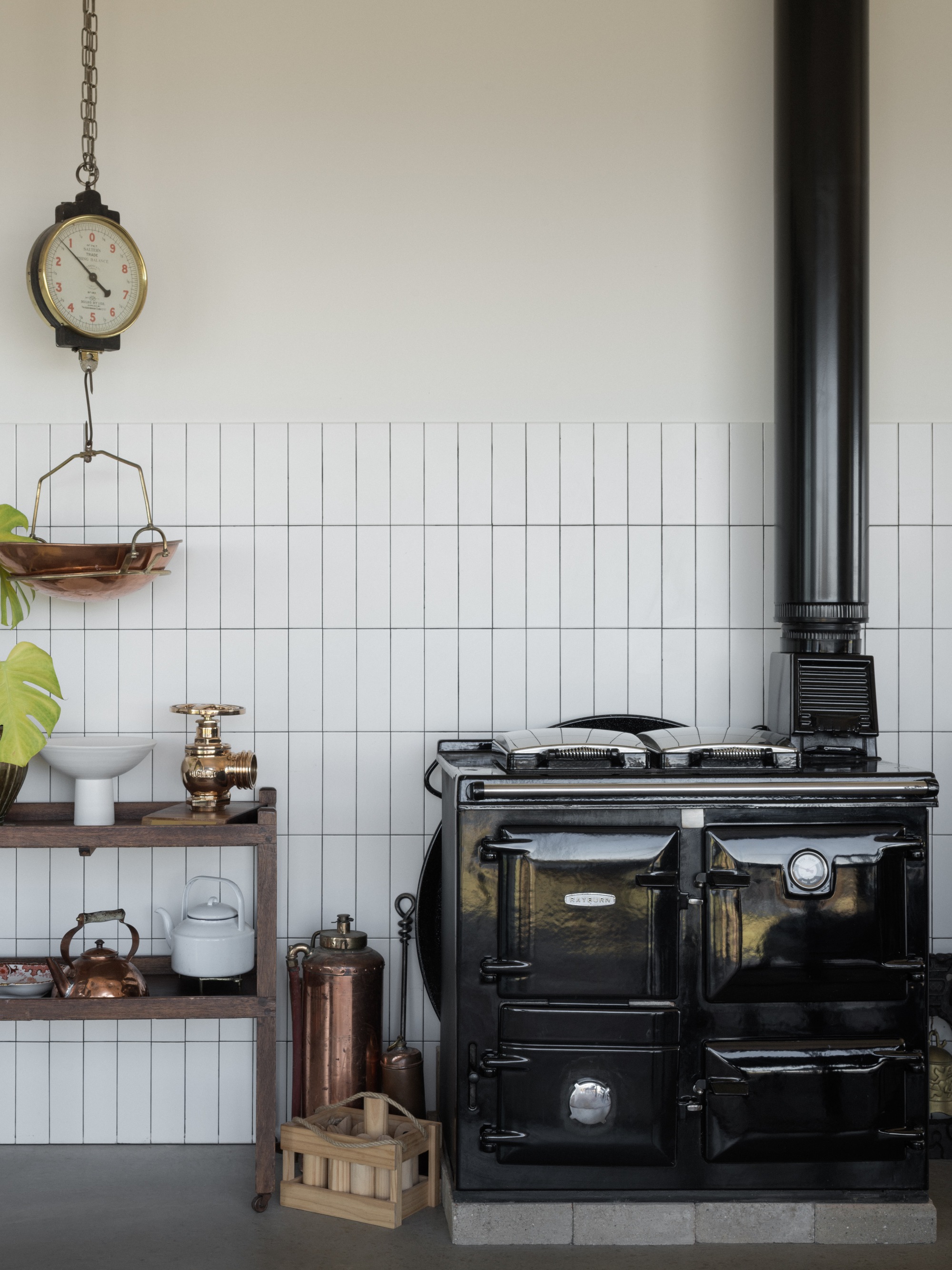 Black cast-iron range against white vertical tile wall with hanging scale and timber shelving