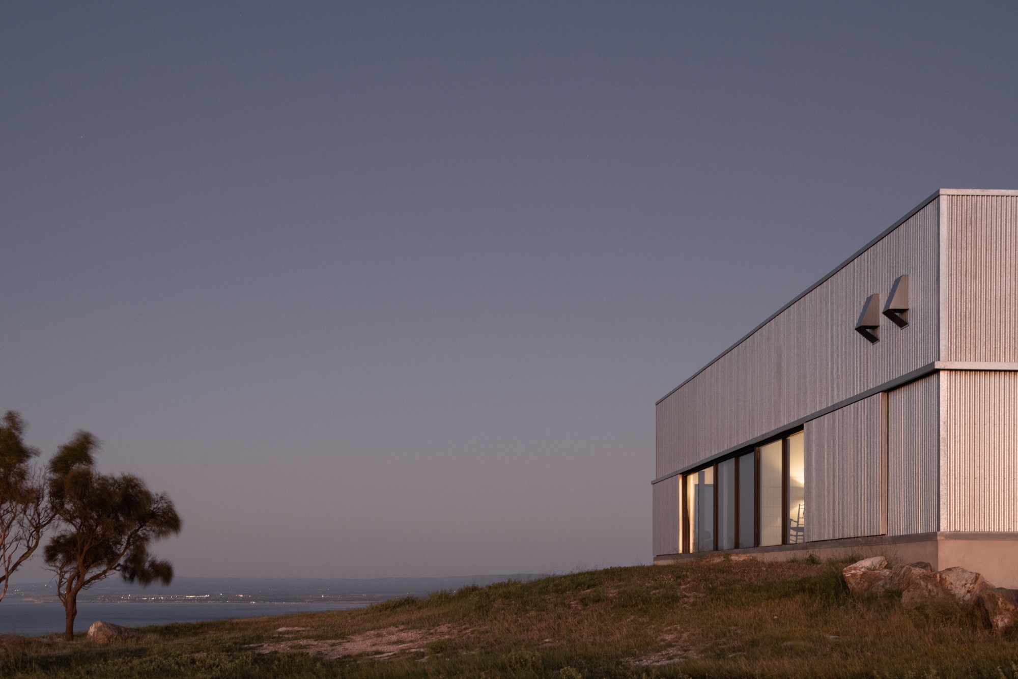 Vertical timber-clad facade with illuminated glazing at twilight facing the coastline