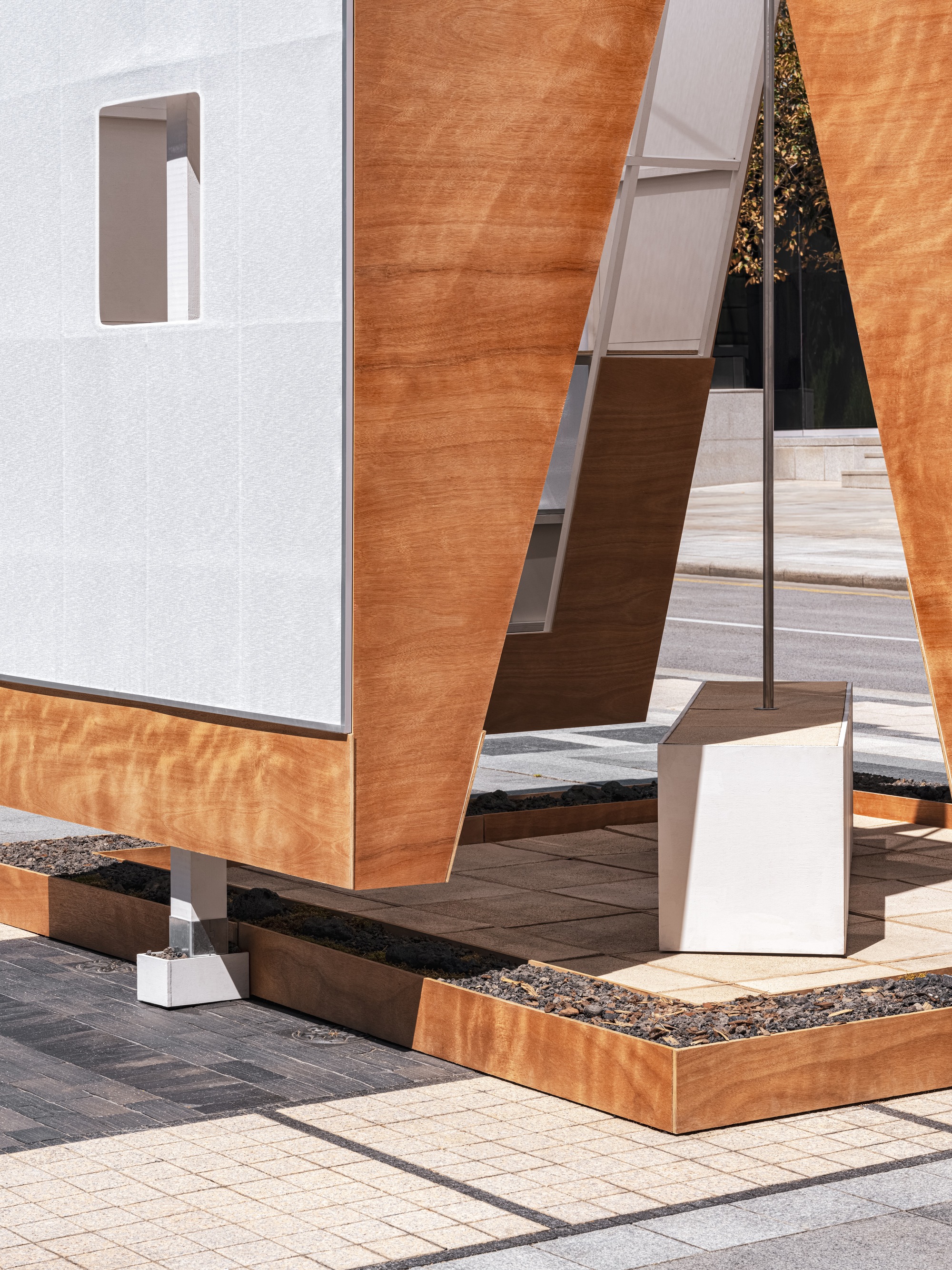 Ground-level detail of laminated timber panels on white metal posts with a black aggregate base