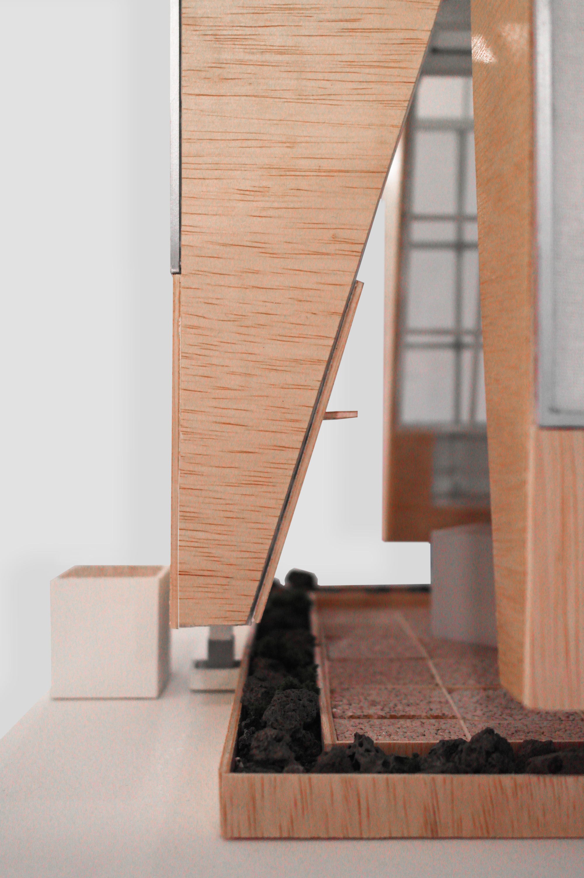 Close-up of a model's angled timber facade panel with black gravel plinth