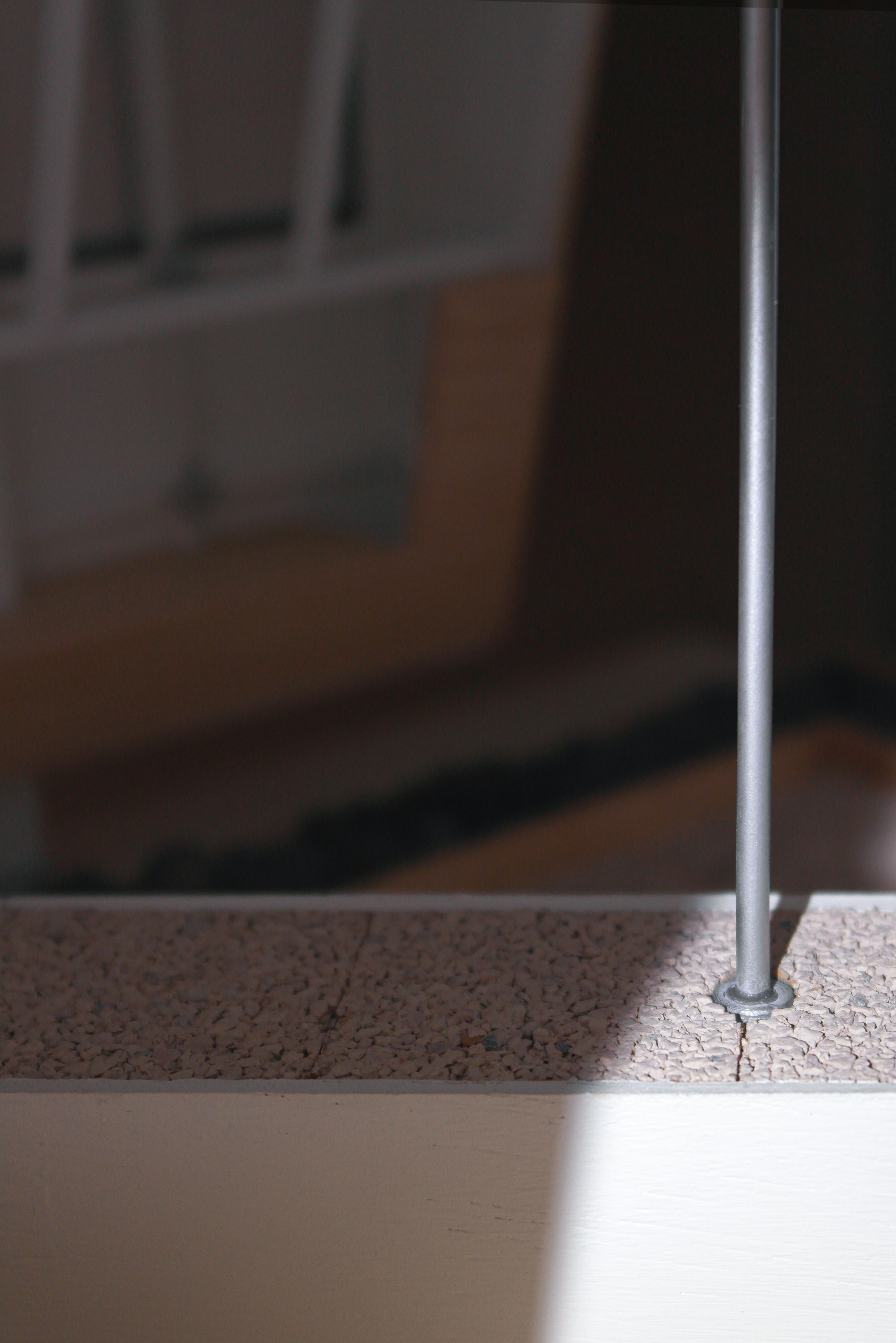 Detail of a slender steel rod anchored into a speckled terrazzo floor