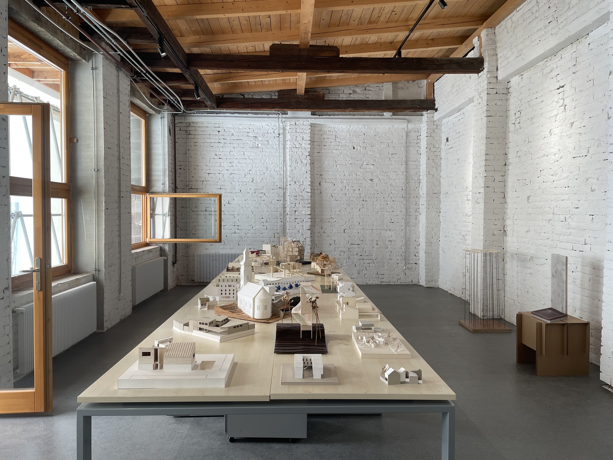 Interior studio space with white painted brick walls, exposed timber ceiling and architectural models on a central table