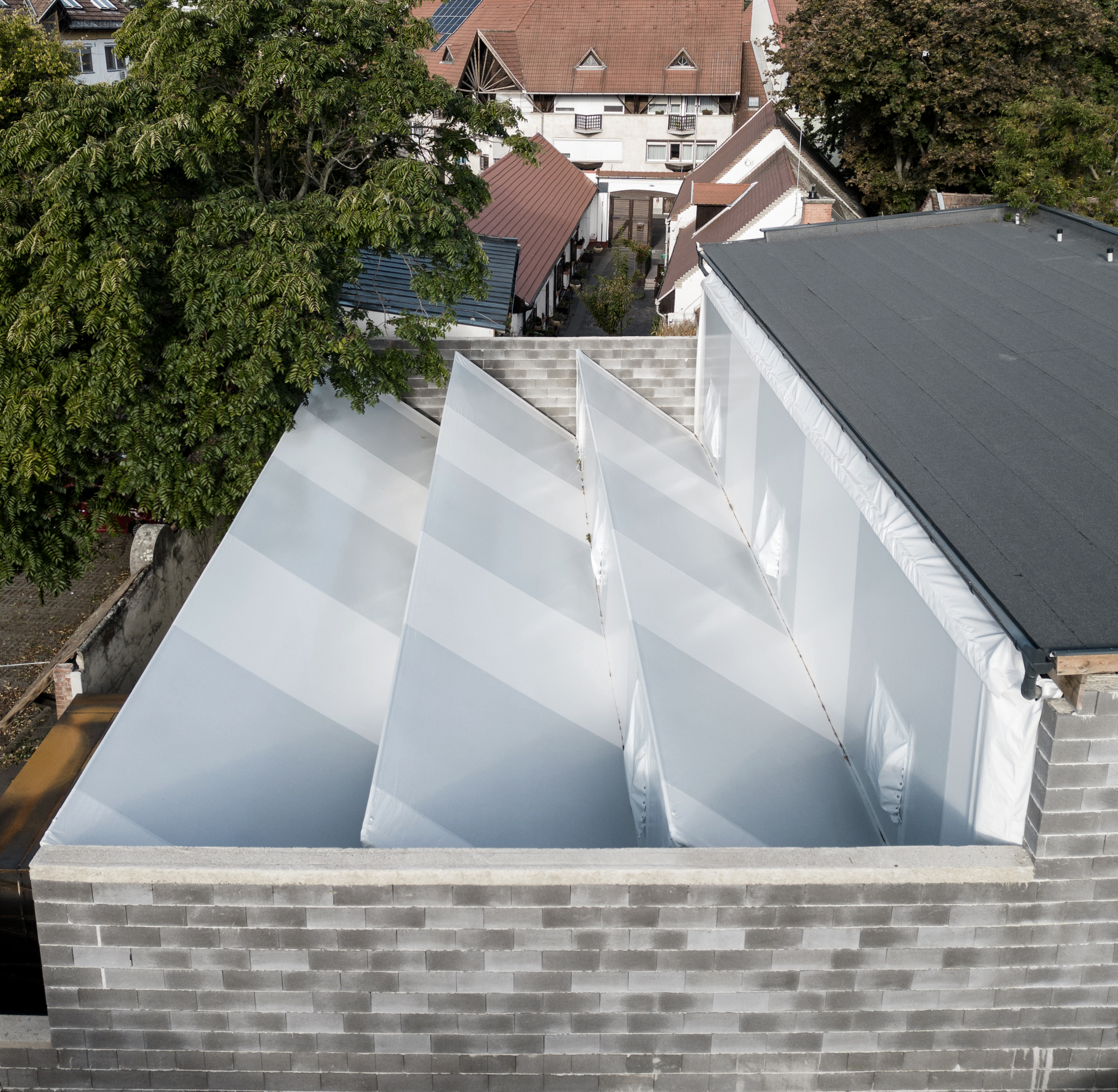 Aerial view of sawtooth skylight structure with white translucent panels atop a patterned brick parapet wall