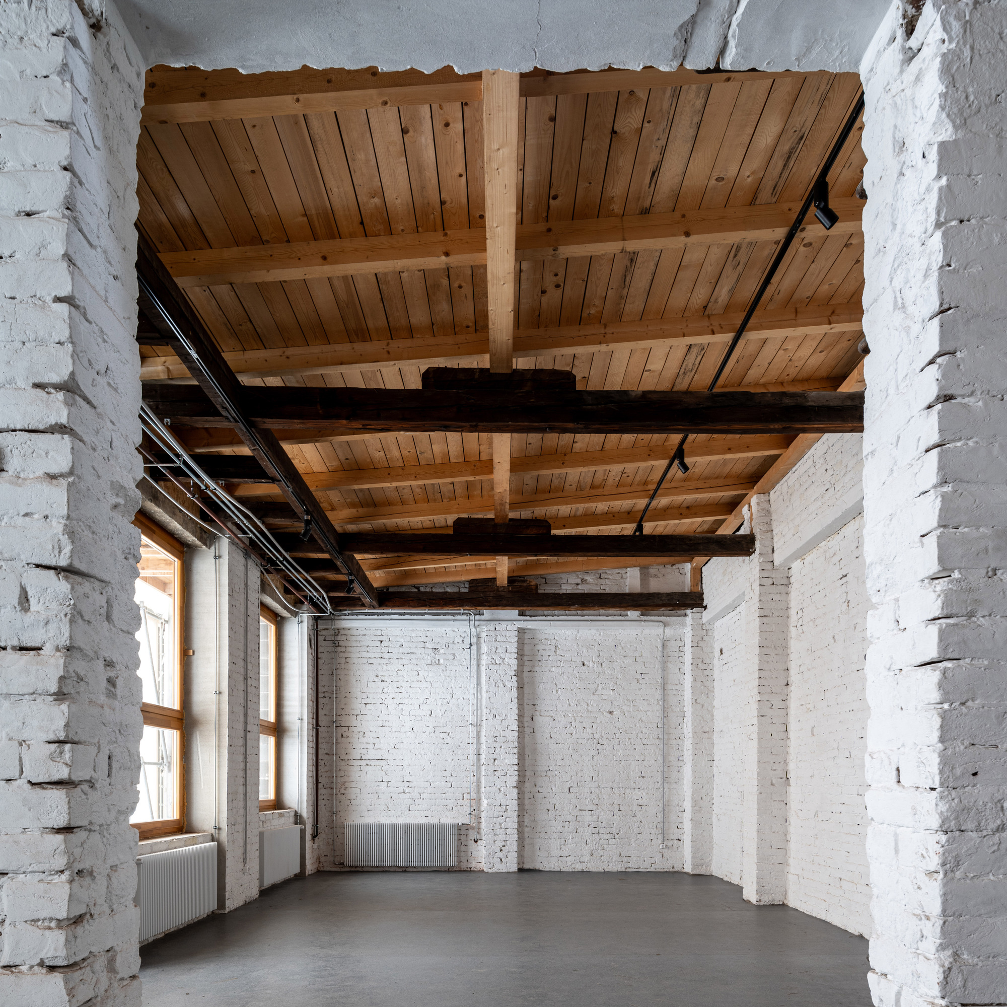 White painted brick interior room with exposed timber plank ceiling and dark steel beams spanning overhead