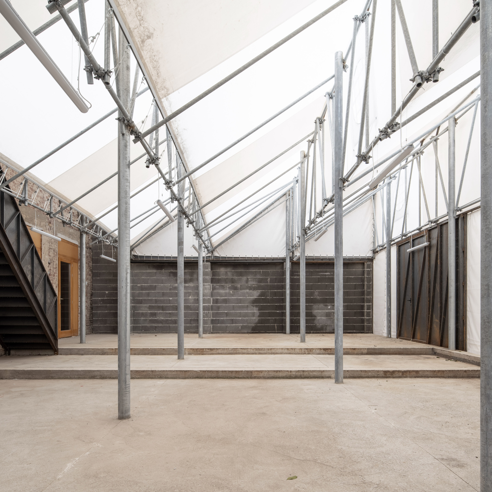 Interior courtyard with galvanized steel structural frame supporting a translucent roof over concrete block walls