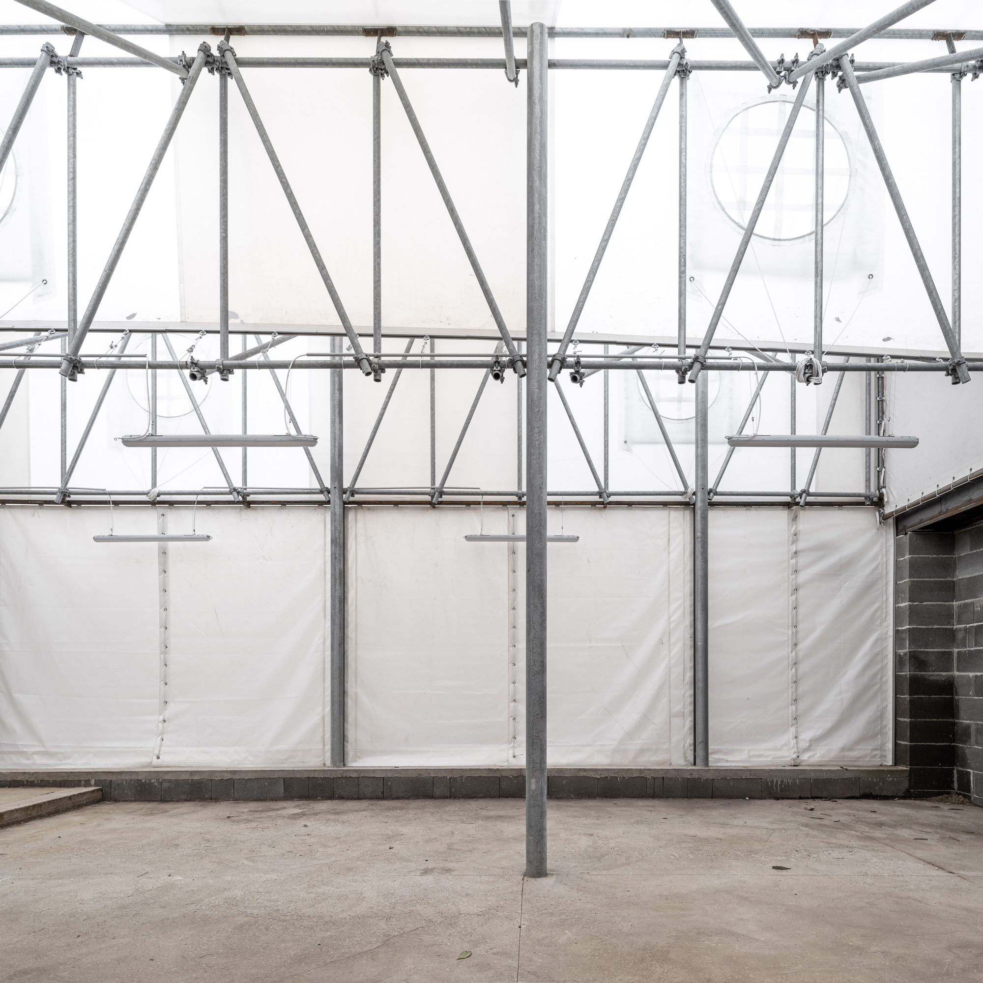 Interior courtyard with galvanized scaffolding frame supporting white tarp enclosure under diffused daylight