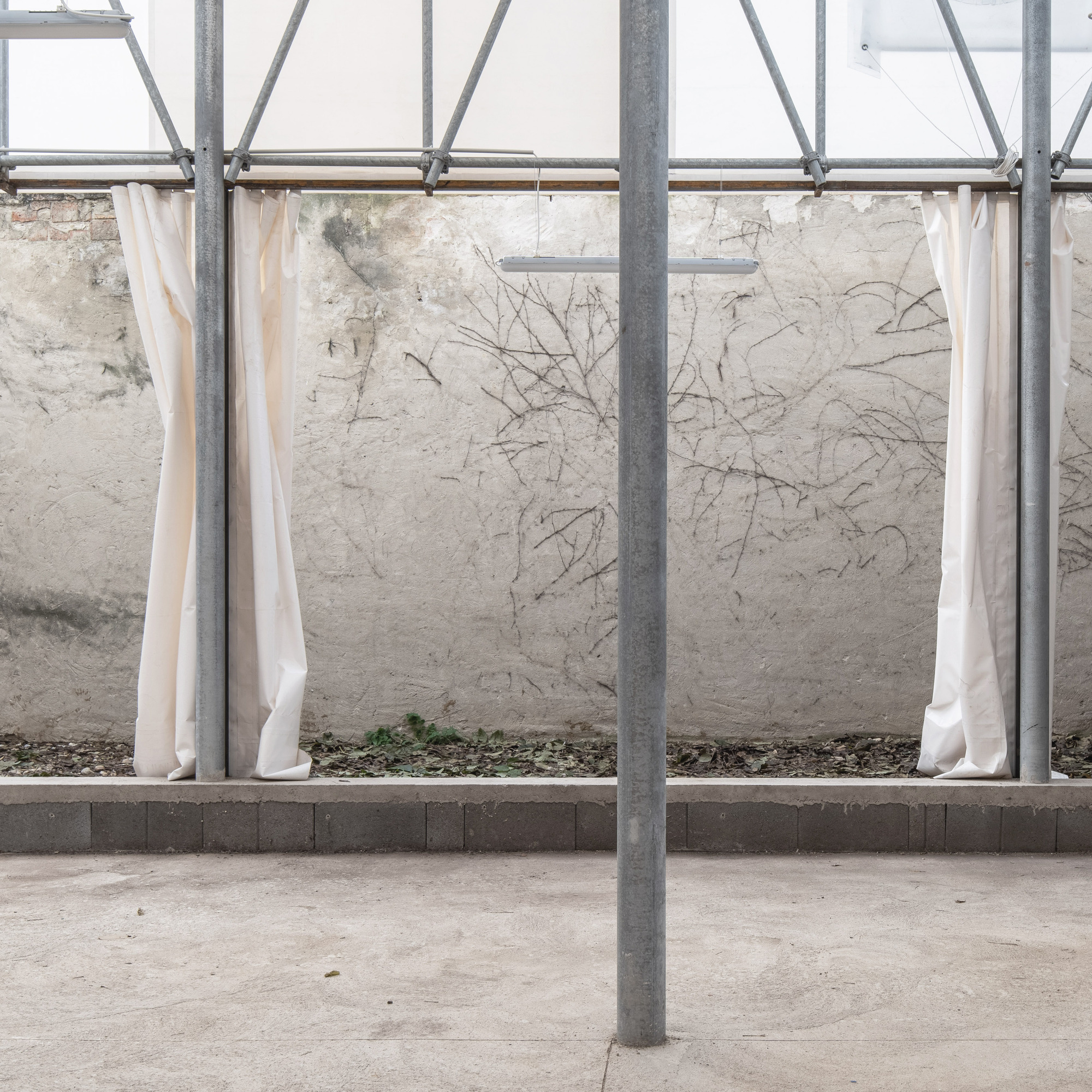 Scaffolding framework with cream fabric curtains suspended along cracked plaster wall on concrete base