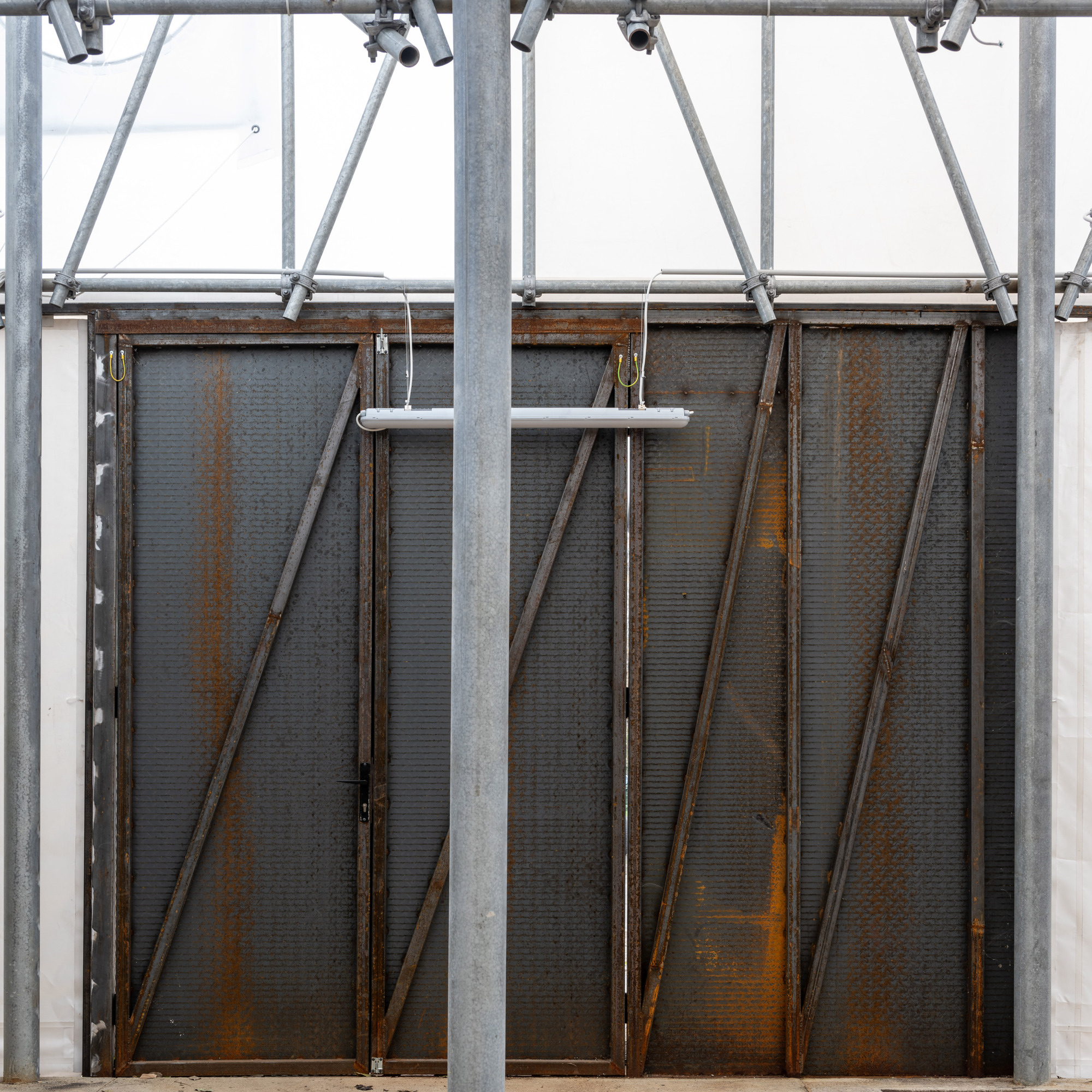 Weathered steel panel doors with diagonal bracing suspended beneath galvanized scaffolding structure