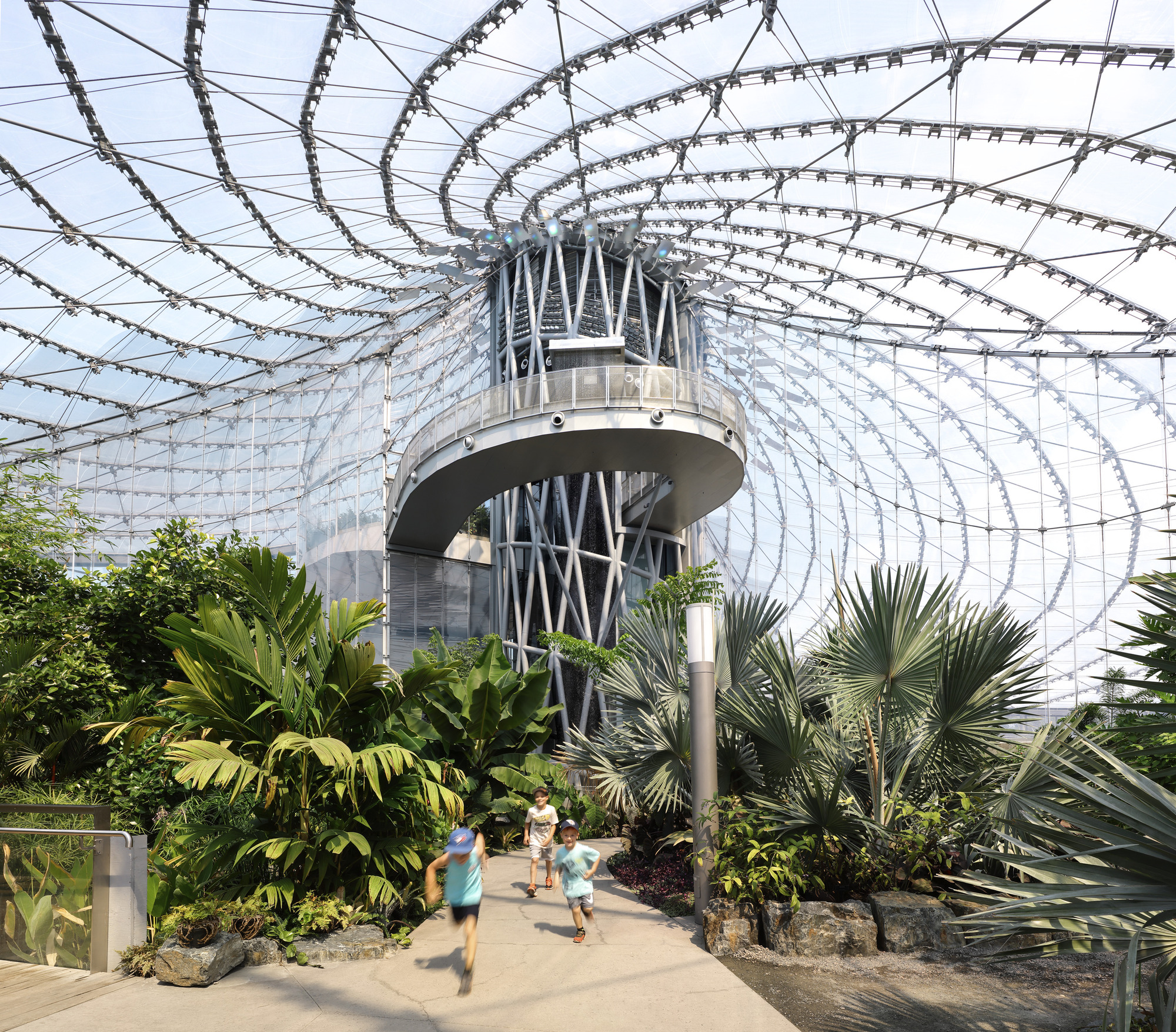 Interior view of the central structural tower beneath the cable roof with tropical palms and children running