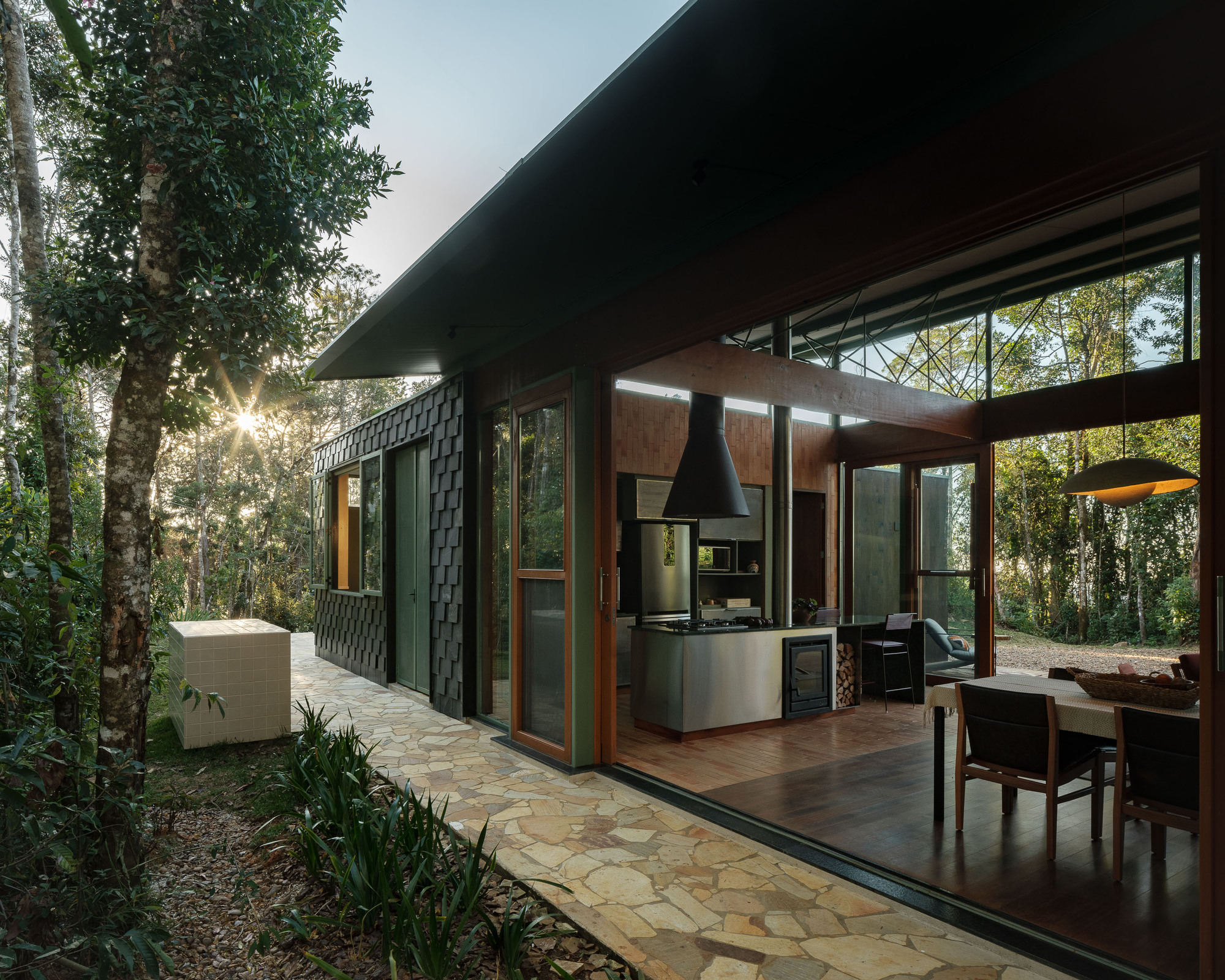 Covered terrace with timber framing and stone paving opening to a kitchen beneath a deep eave at dusk