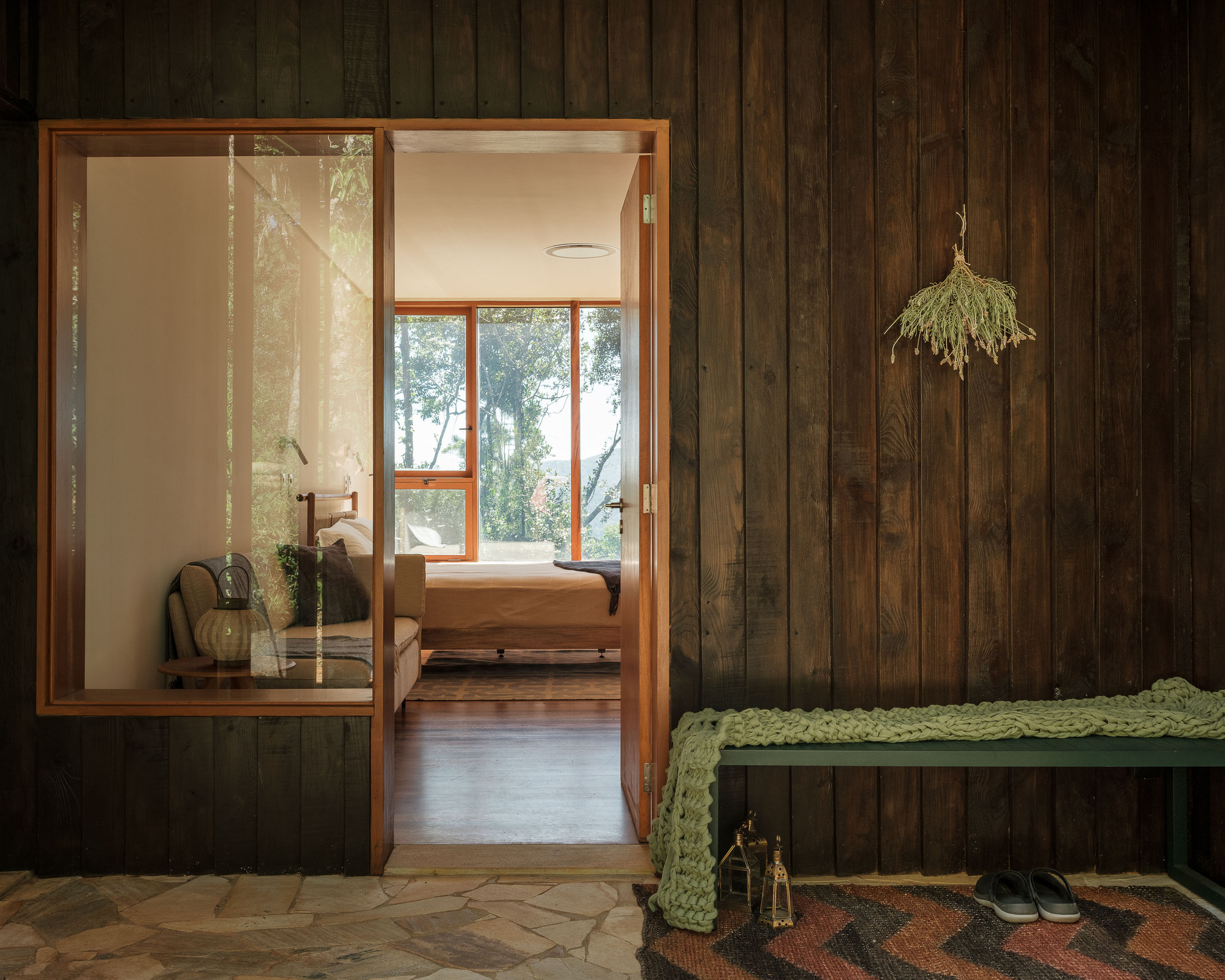 Timber-clad entry vestibule with sliding glass door opening to interior bedroom with forest views