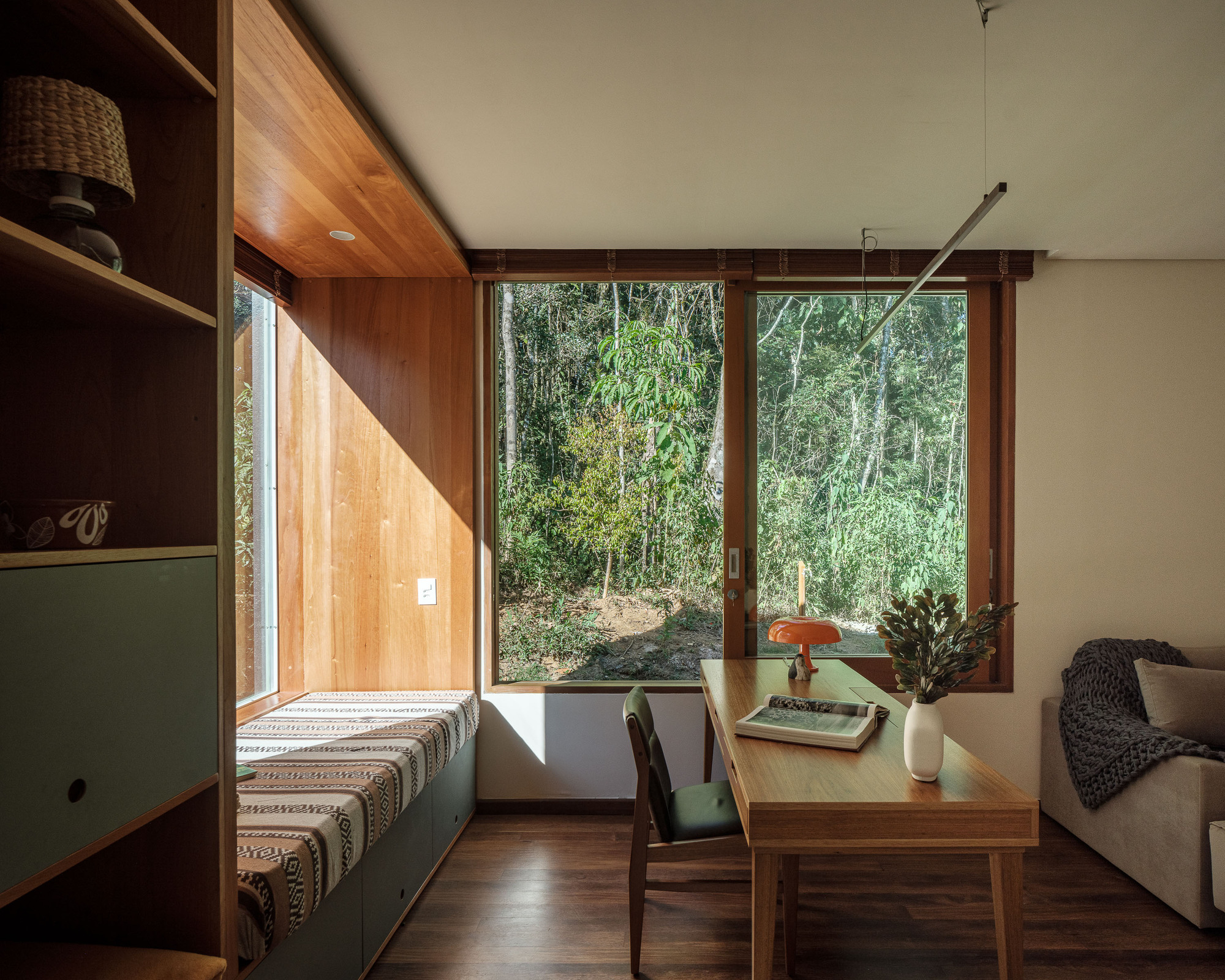 Interior living space with corner windows overlooking bamboo grove and built-in seating along timber wall