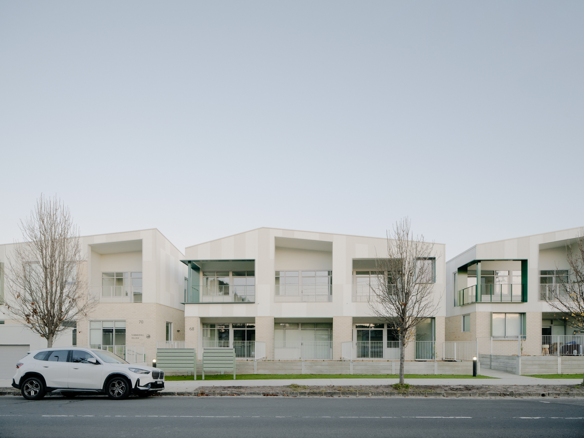 Street view of white residential facade with recessed balconies and young winter trees