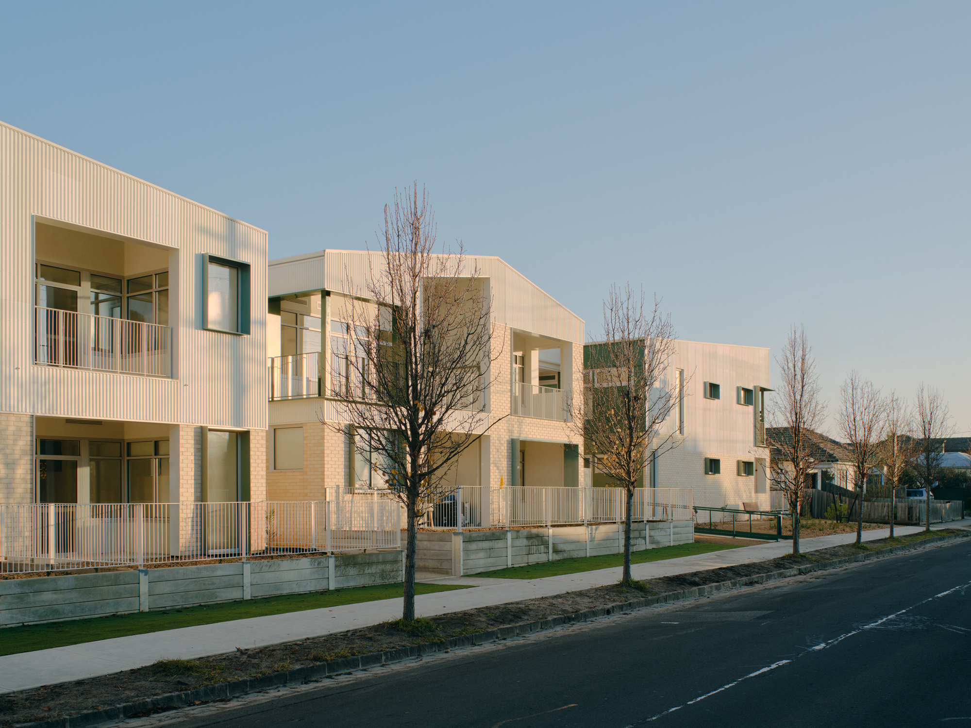 Angled street view of the housing complex with repeating volumes along the roadway in afternoon light