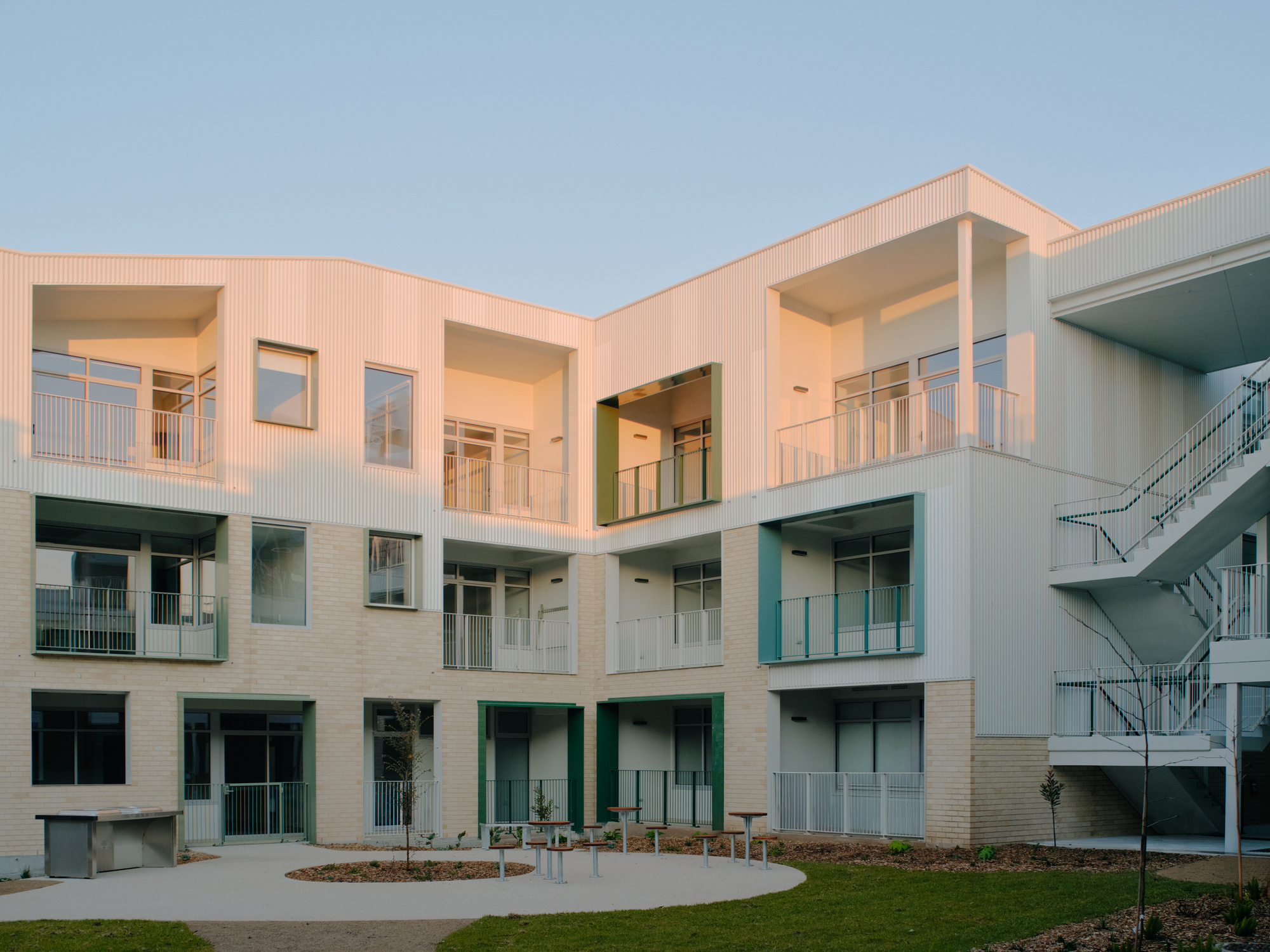 Courtyard view showing tiered balconies, exterior stairs and planted lawn under evening sky