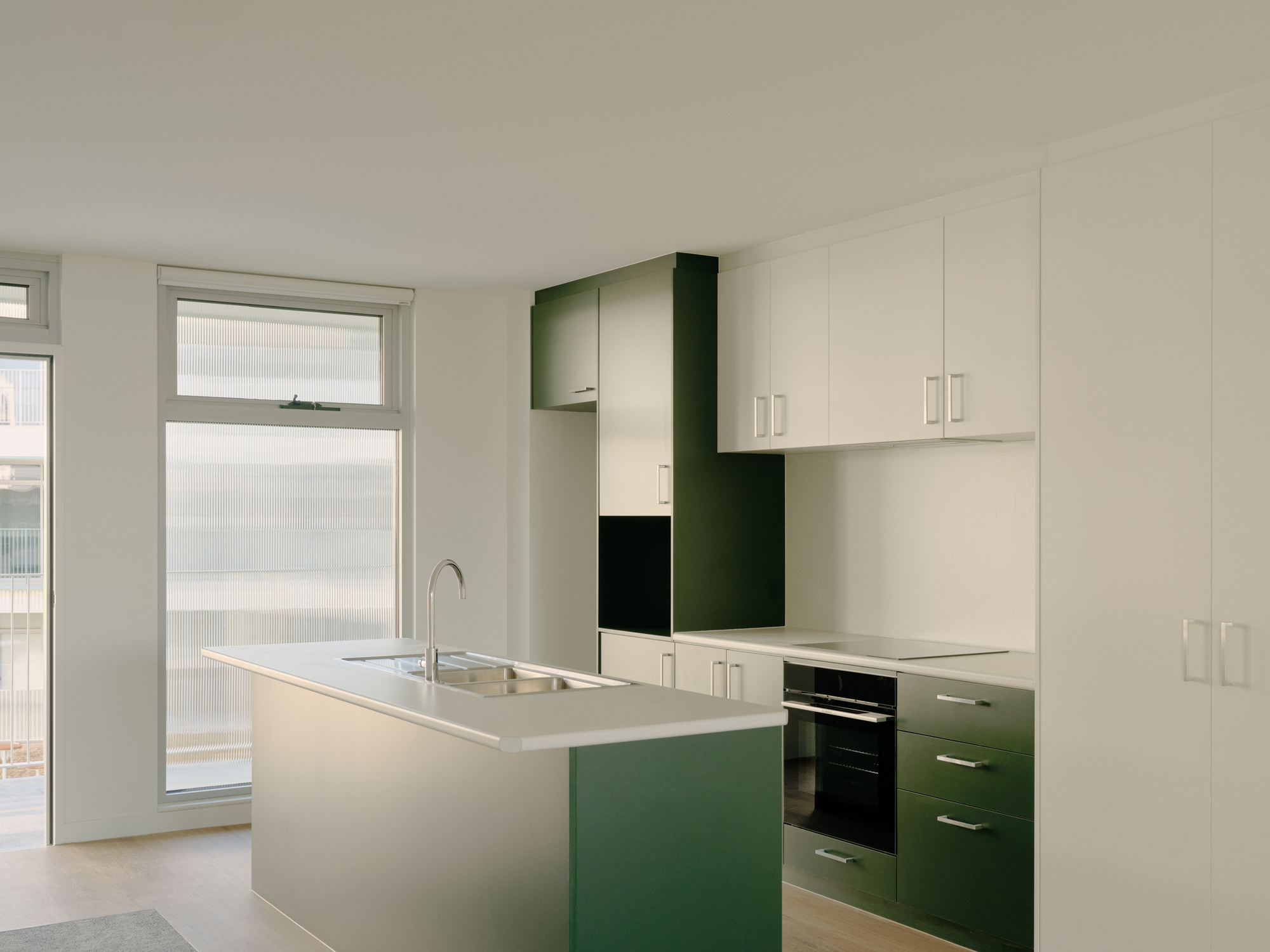 Kitchen interior with green and white cabinetry, island bench and balcony door with translucent glazing