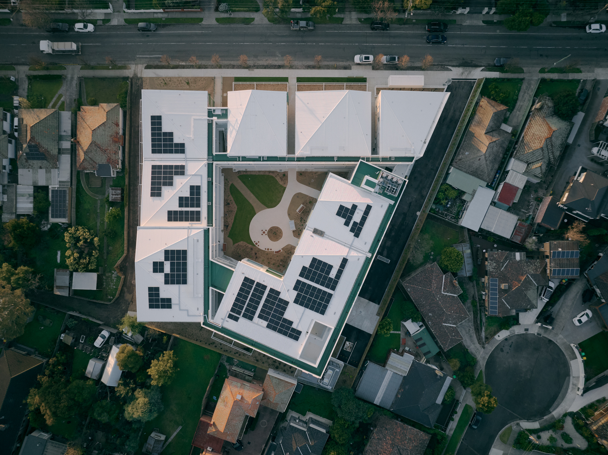 Aerial view of flat rooftops with solar panel arrays and shared courtyard gardens in a dense urban neighborhood