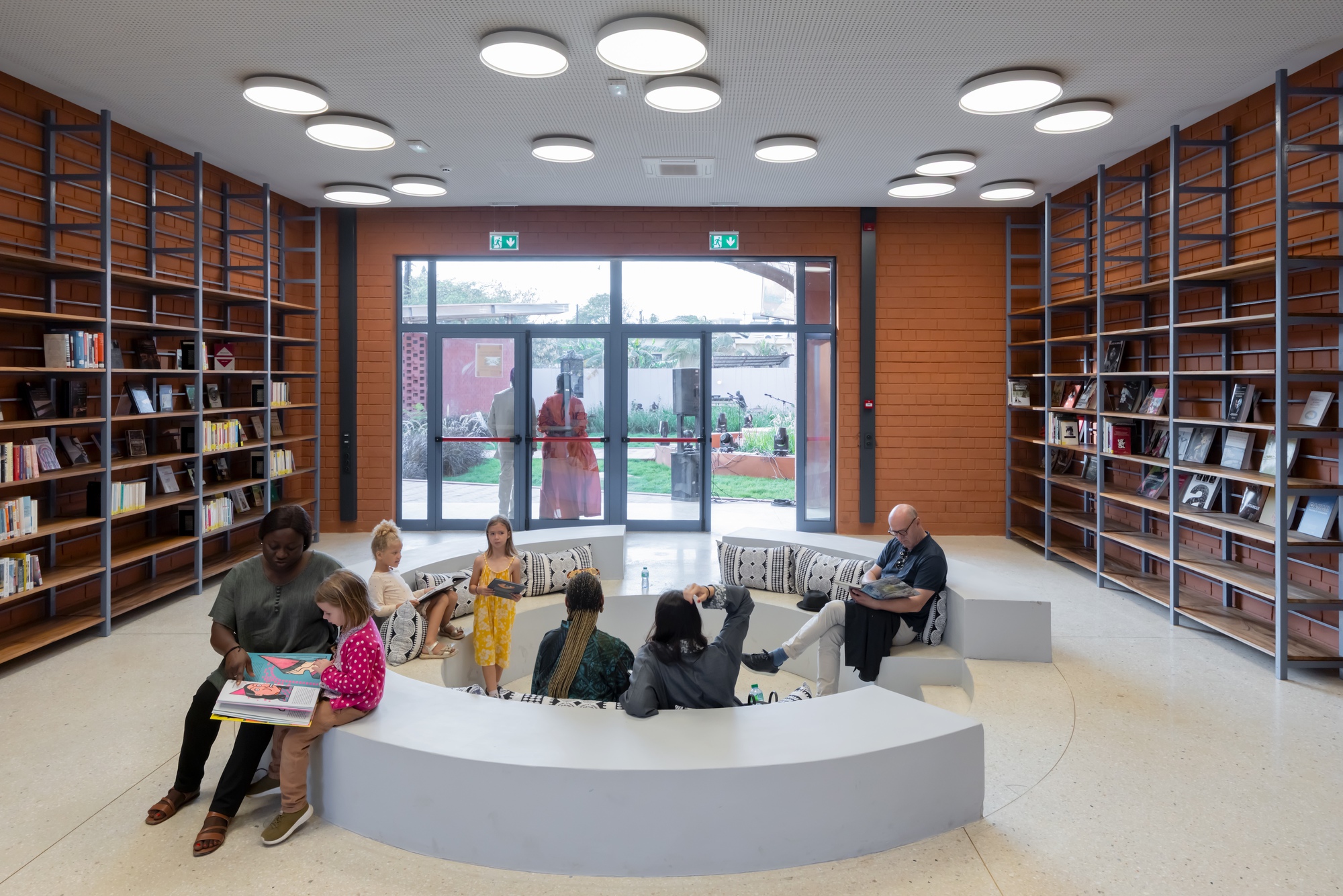 Reading room with circular seating platform, timber bookshelves, and visitors beneath clustered ceiling lights