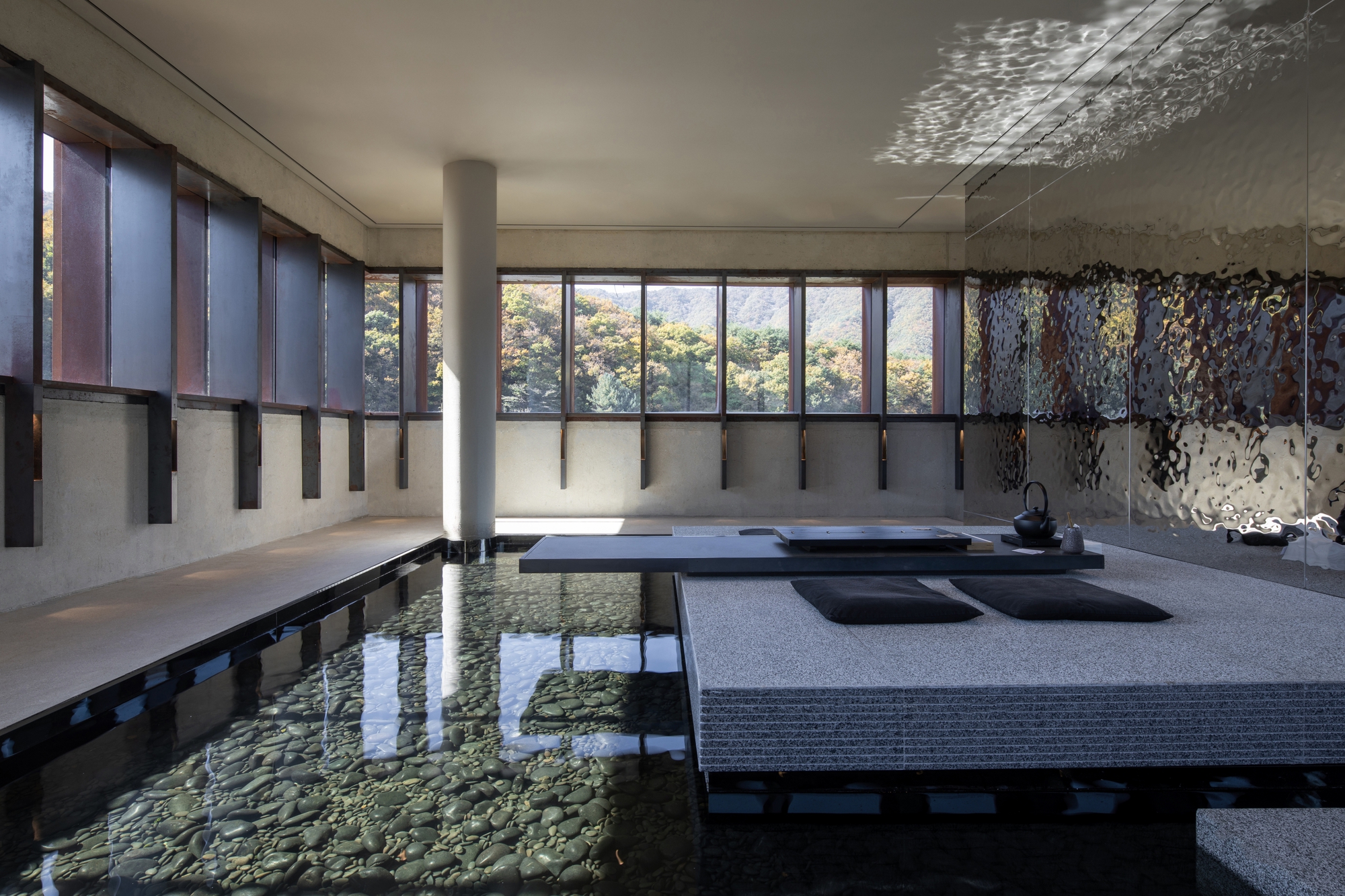 Interior reflecting pool with raised seating platforms beneath glazed clerestory and dappled light on the ceiling