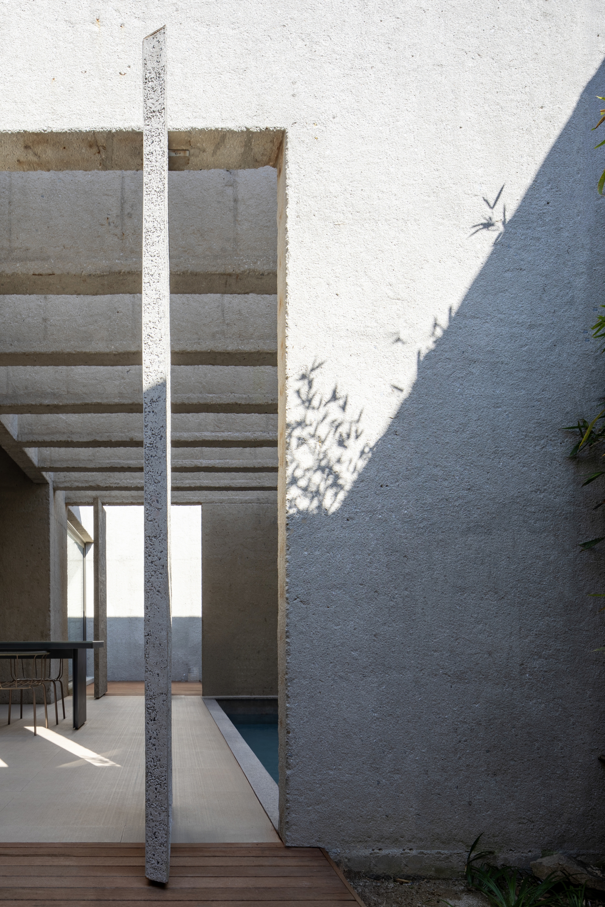 View through a slatted concrete pergola casting crisp shadows on a white textured wall