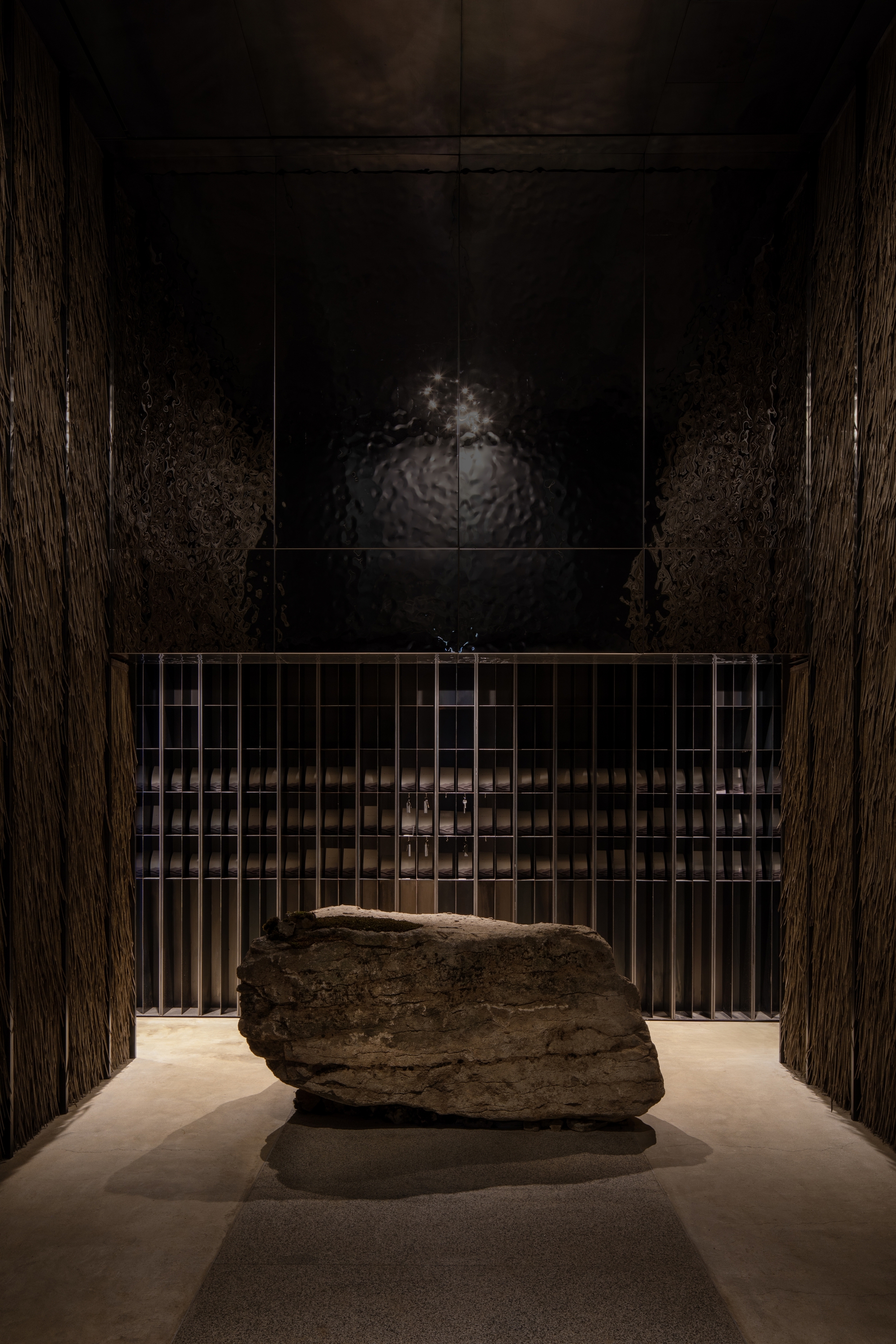 Entry hall with large stone boulder on plinth behind metal grille and dark wood paneling