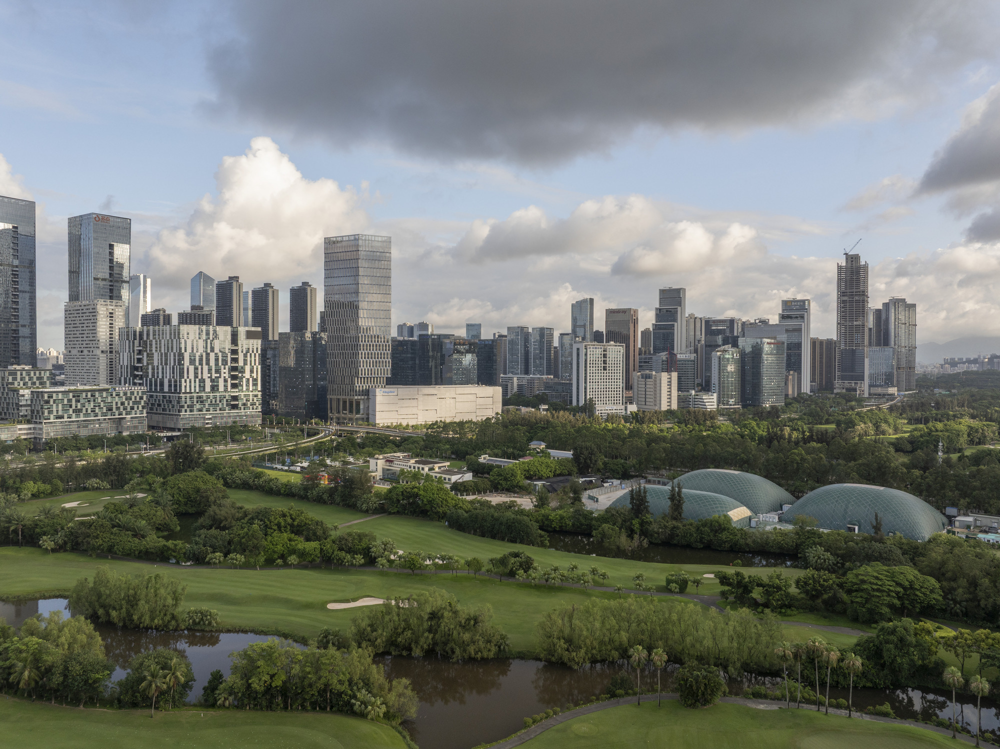 Skyline view showing tower and domed glass structures set within parkland under cloudy skies