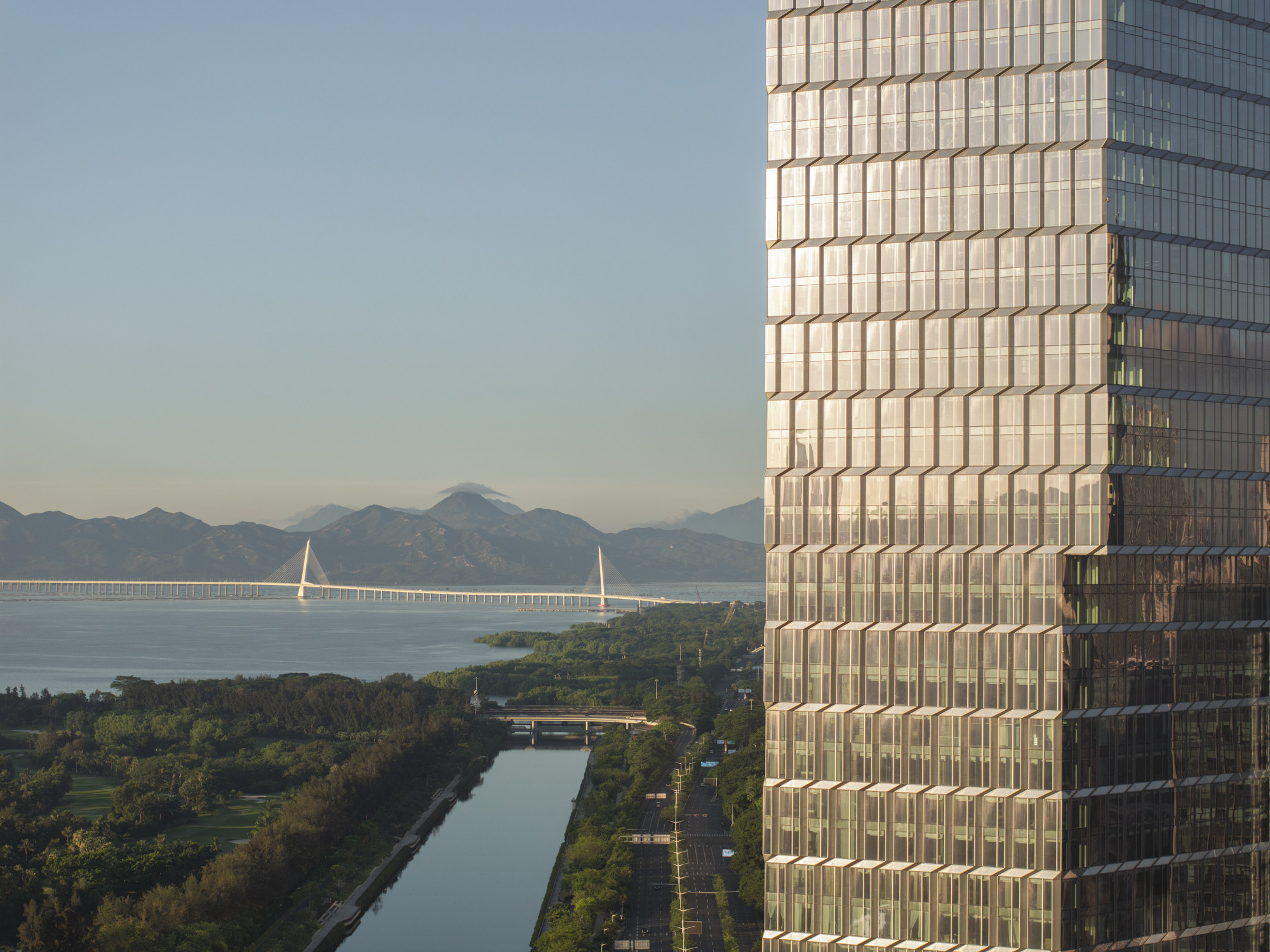 Close-up of gridded glass facade overlooking waterway with cable-stayed bridge and distant mountains