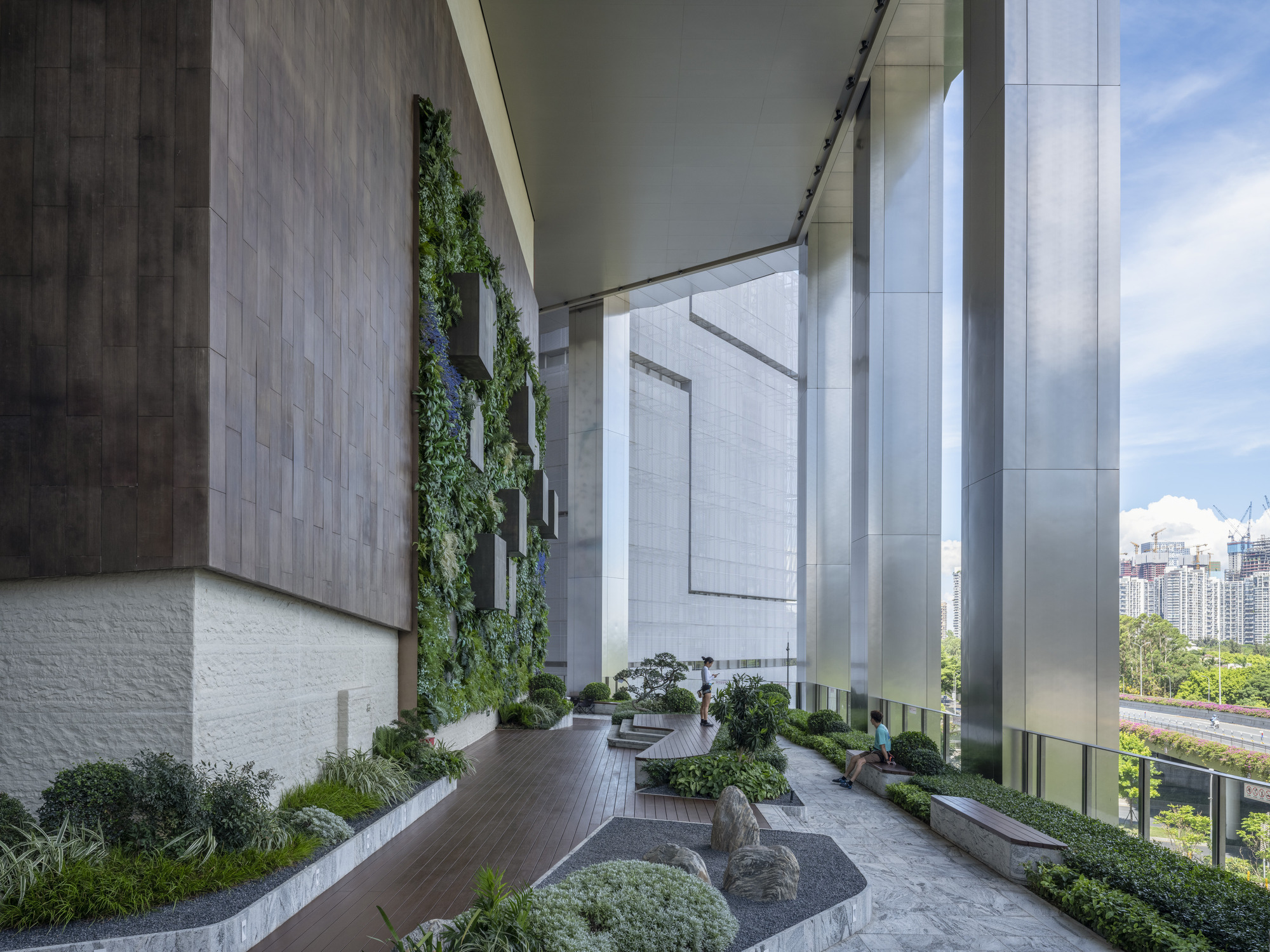 Covered outdoor terrace with planted beds, vertical greenery, and timber decking between tower volumes