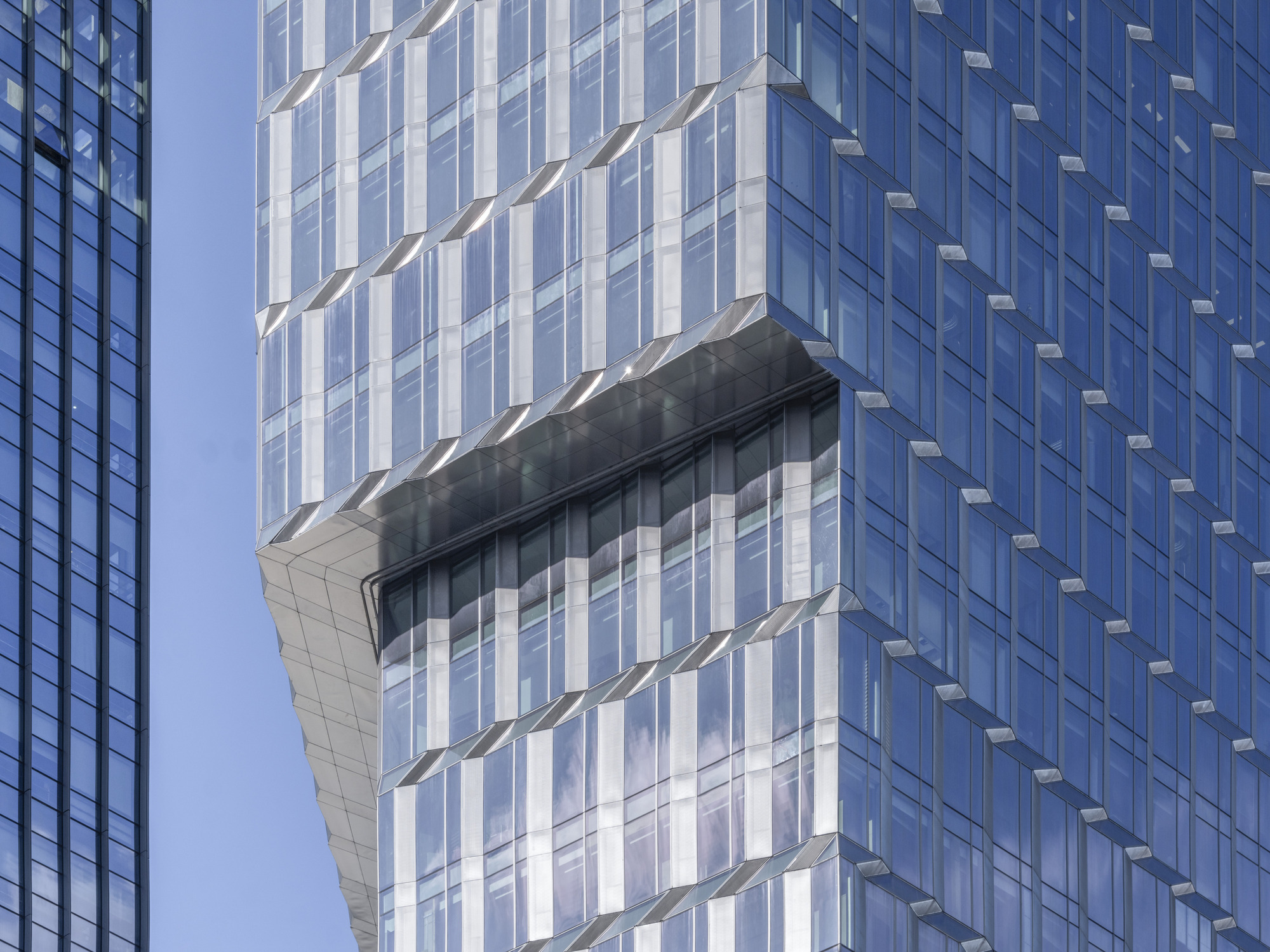 Close-up of the stepped glass tower facade with a protruding horizontal band under clear blue sky