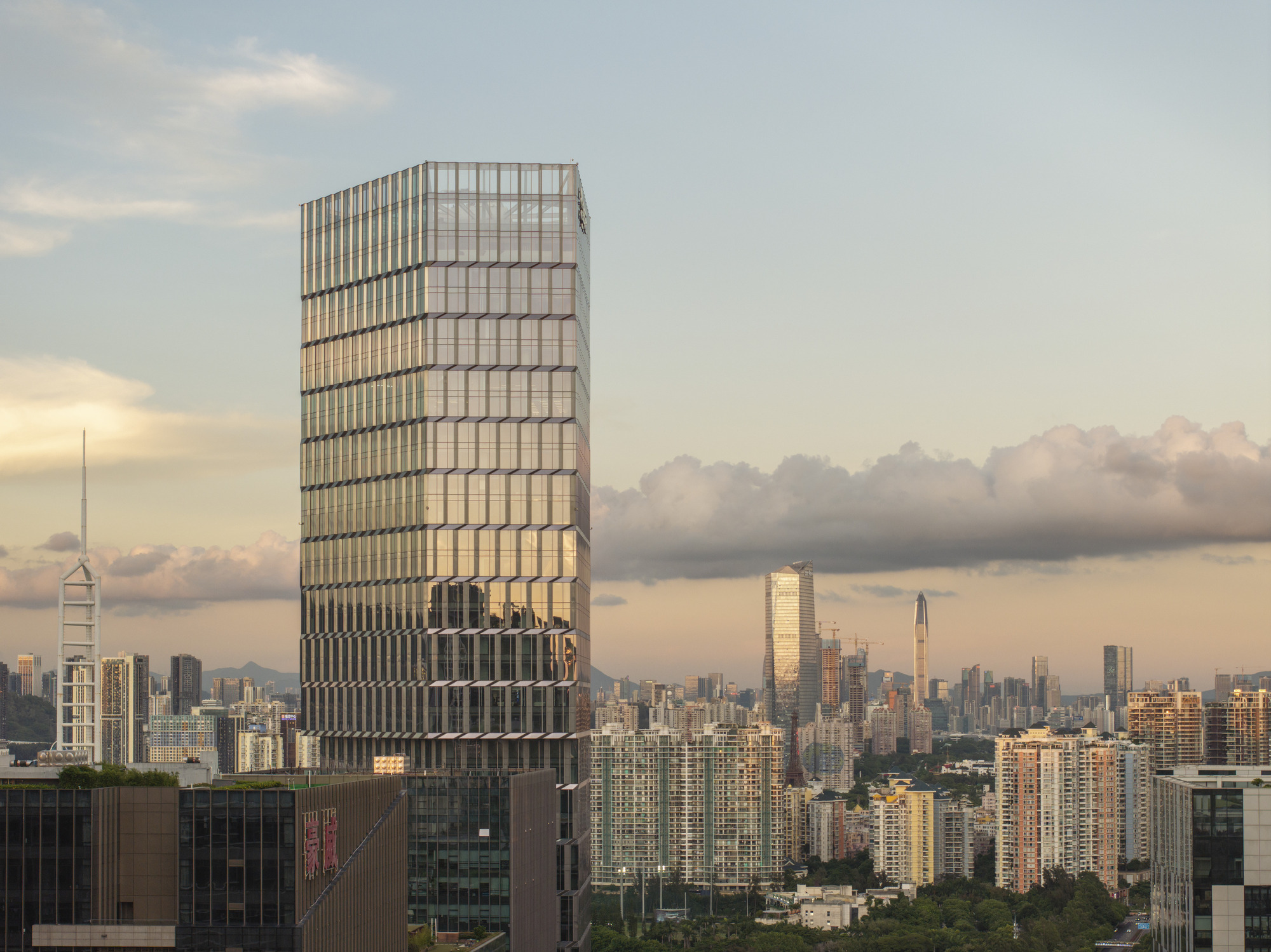 Twisted glass tower rising above the urban skyline at dusk with clouds gathering
