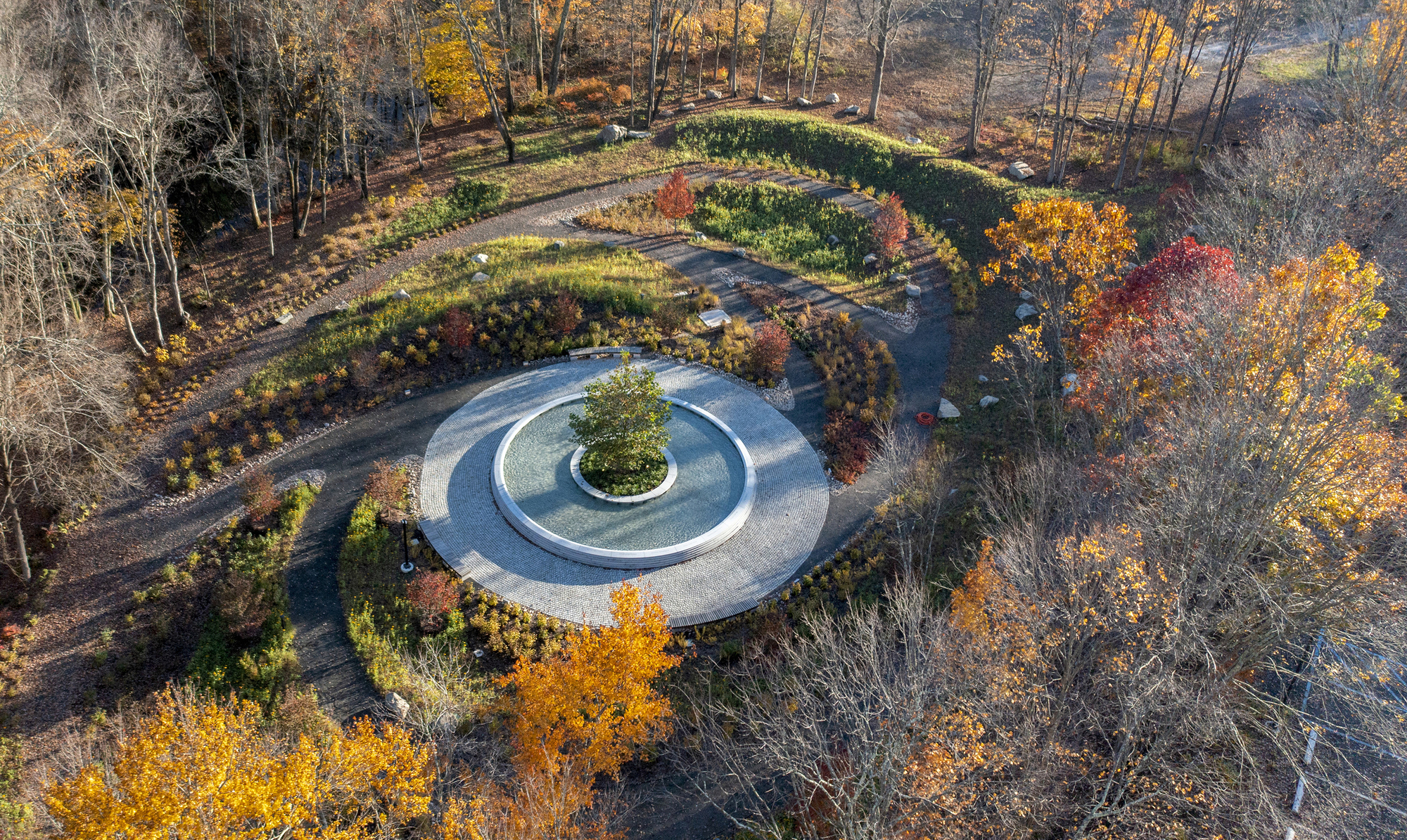 Drone view showing the concentric stone paving rings and curved planted beds in fall color