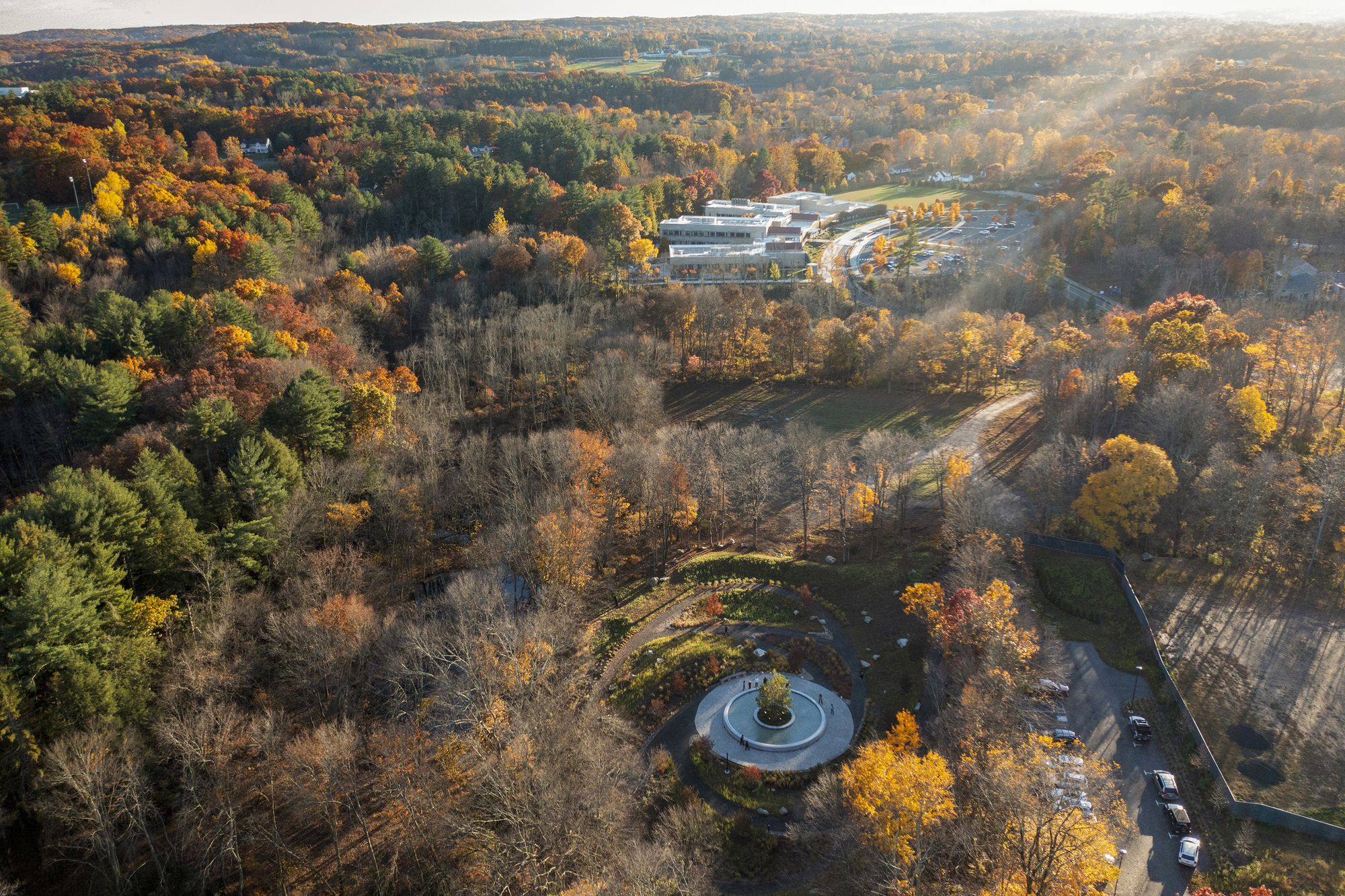 Long aerial view of the plaza in the forested valley with buildings visible in the distance
