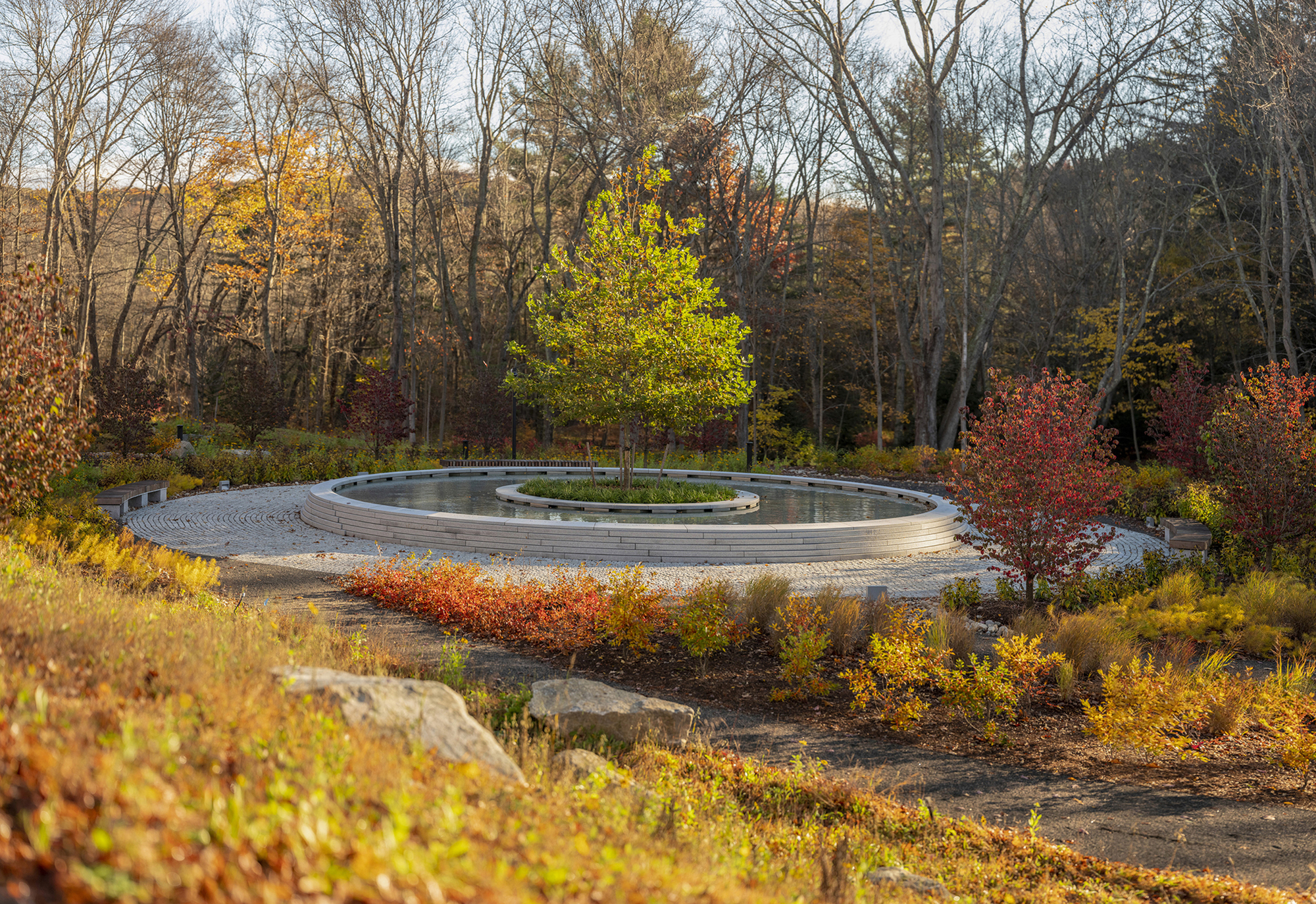 Circular memorial fountain with concentric granite rings and planted island surrounded by autumn foliage