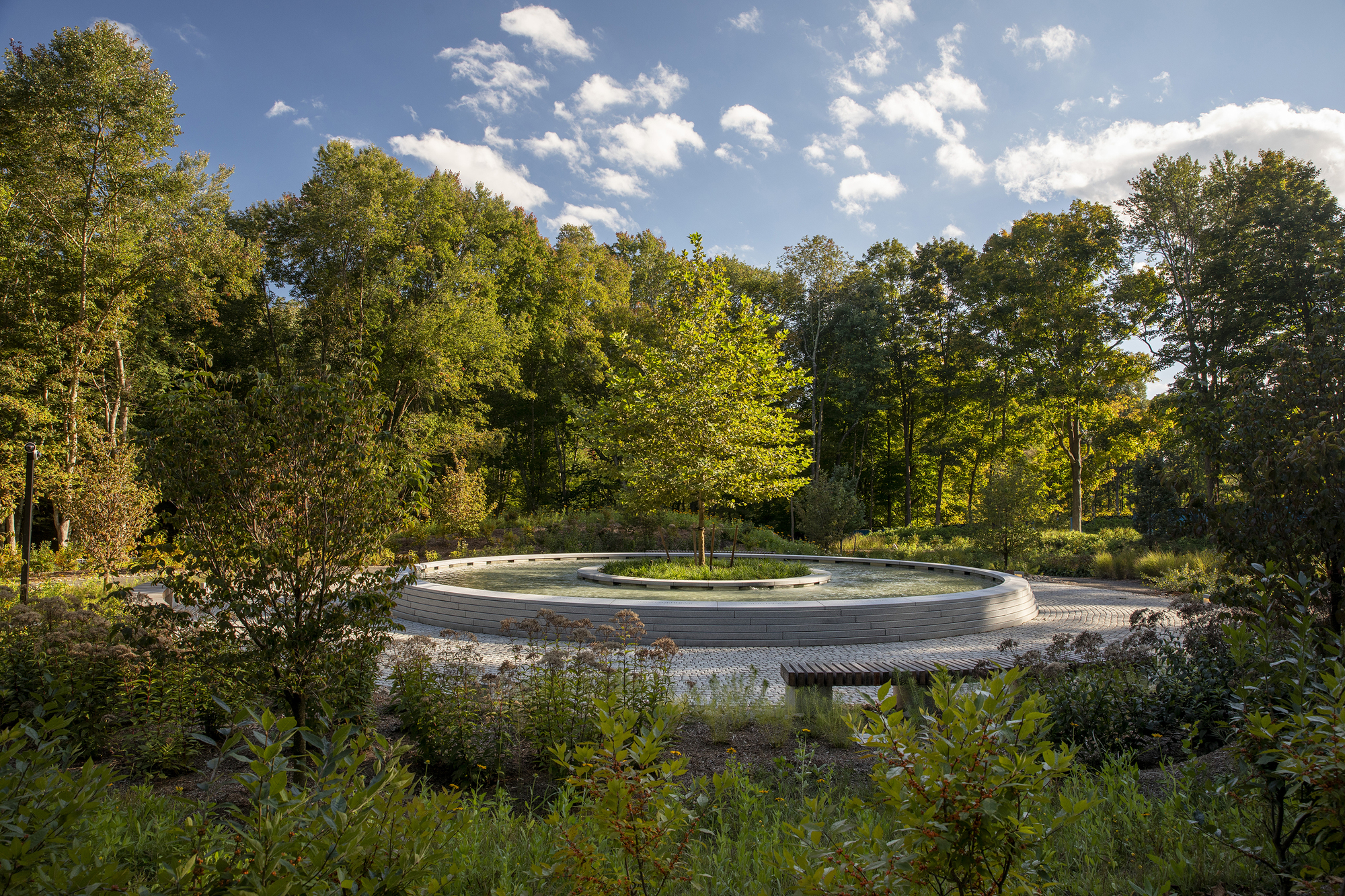 Long view of the circular memorial set within native plantings under a clear blue sky