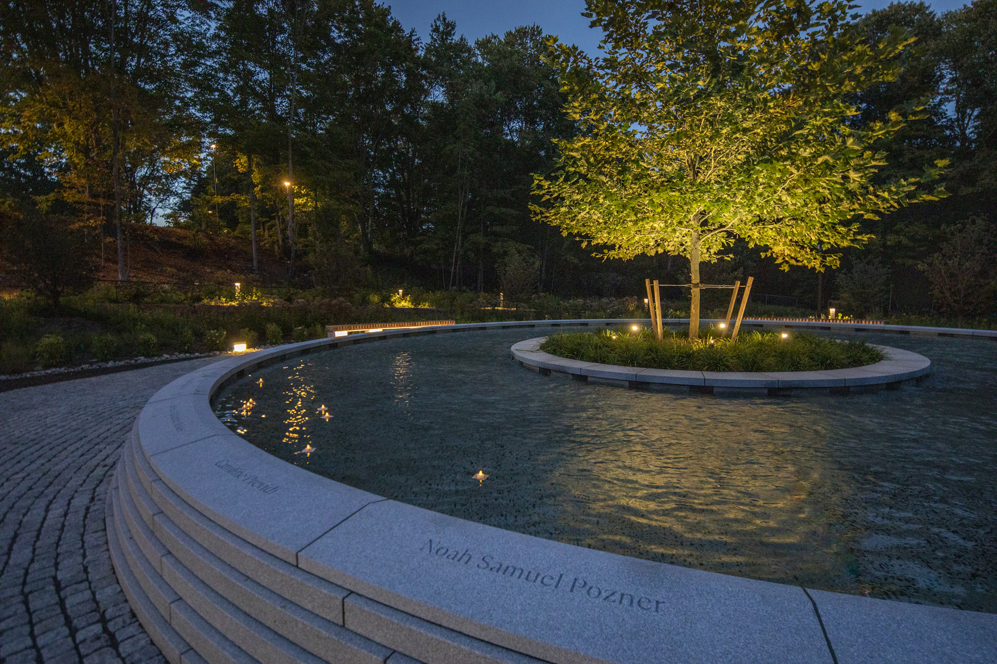 Evening view of the illuminated fountain pools with inscribed coping and lit perimeter planting