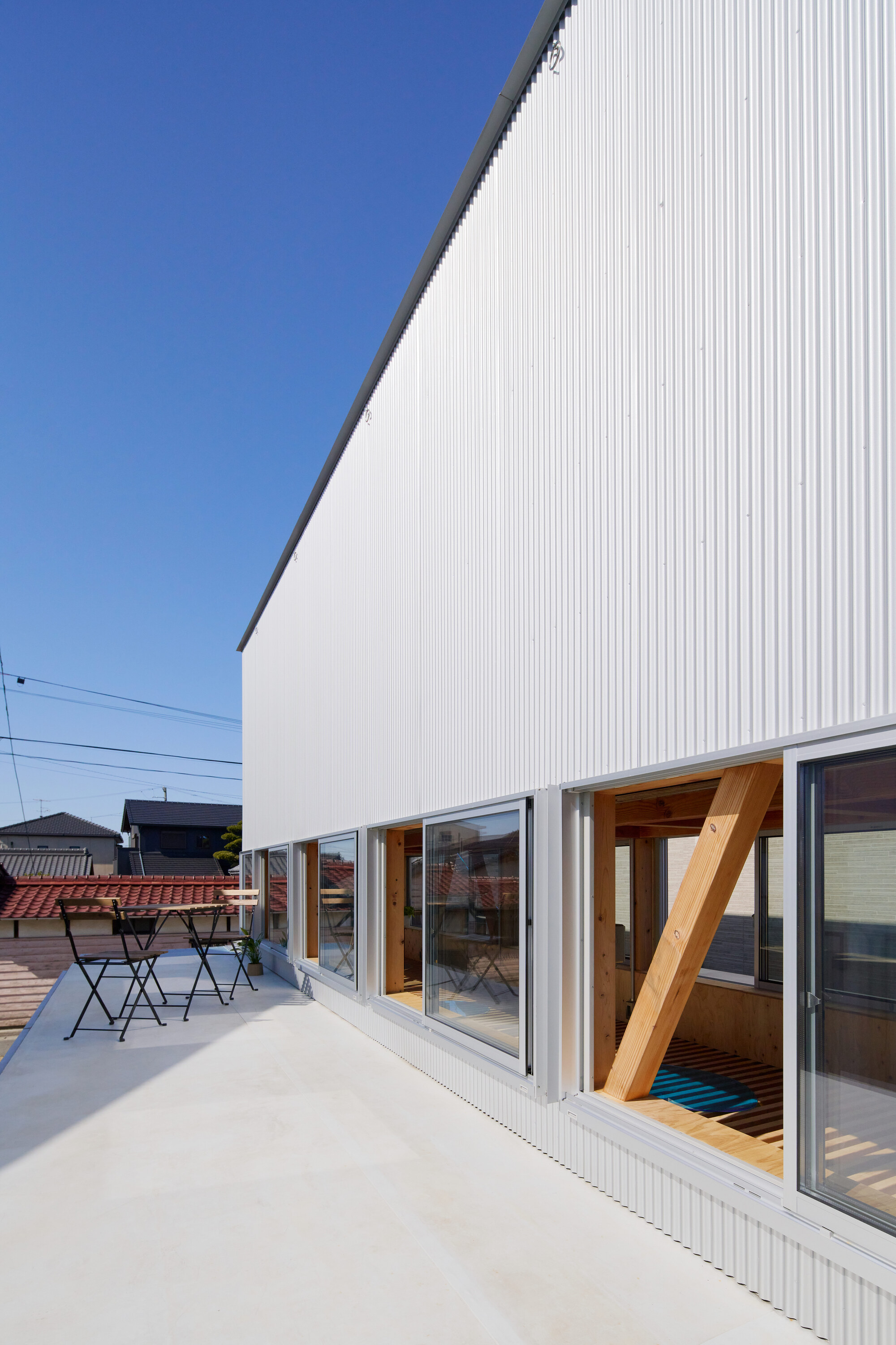 Rooftop terrace with white corrugated metal wall and sliding glass doors revealing timber structure within