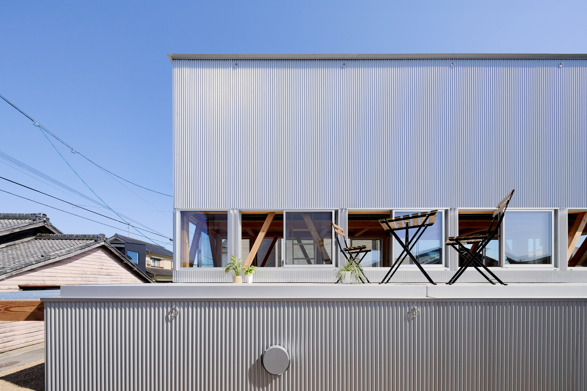 Rooftop terrace with corrugated metal cladding and a pair of folding chairs under clear blue sky