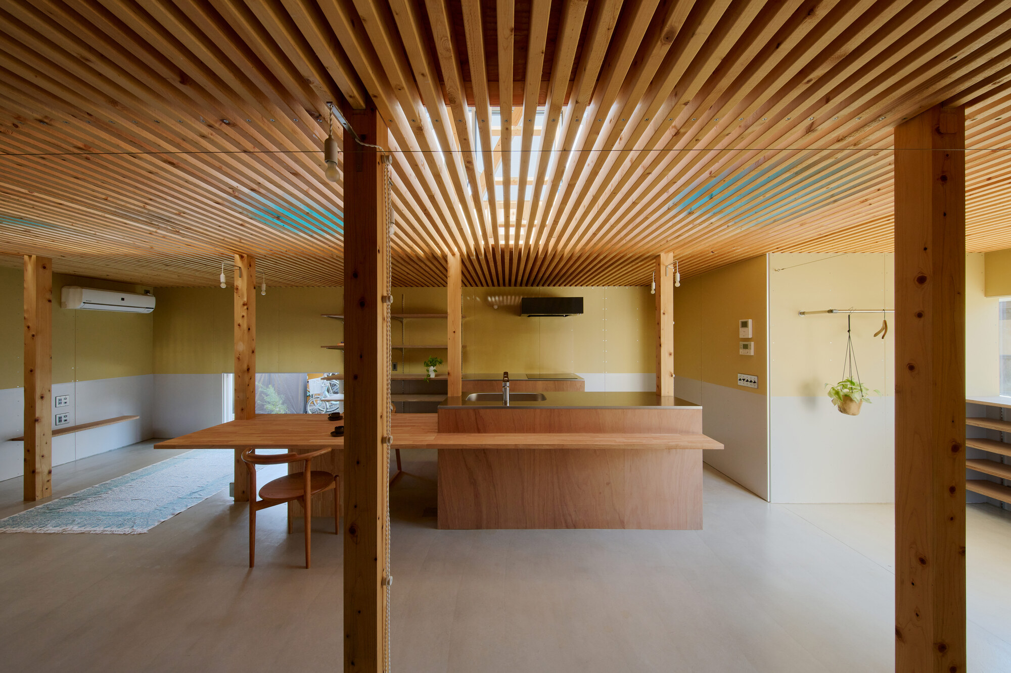 Open plan kitchen and dining space with exposed timber slat ceiling and concrete floor
