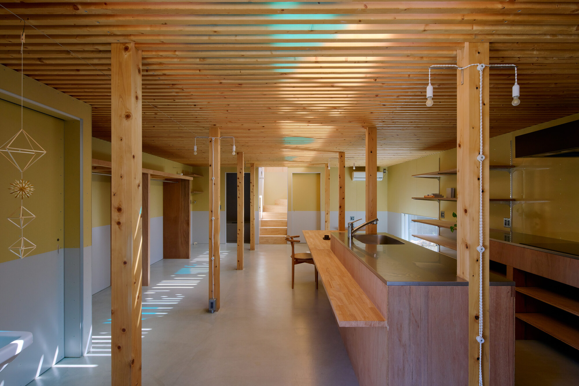 Interior with timber columns and slatted ceiling casting shadow patterns across polished concrete