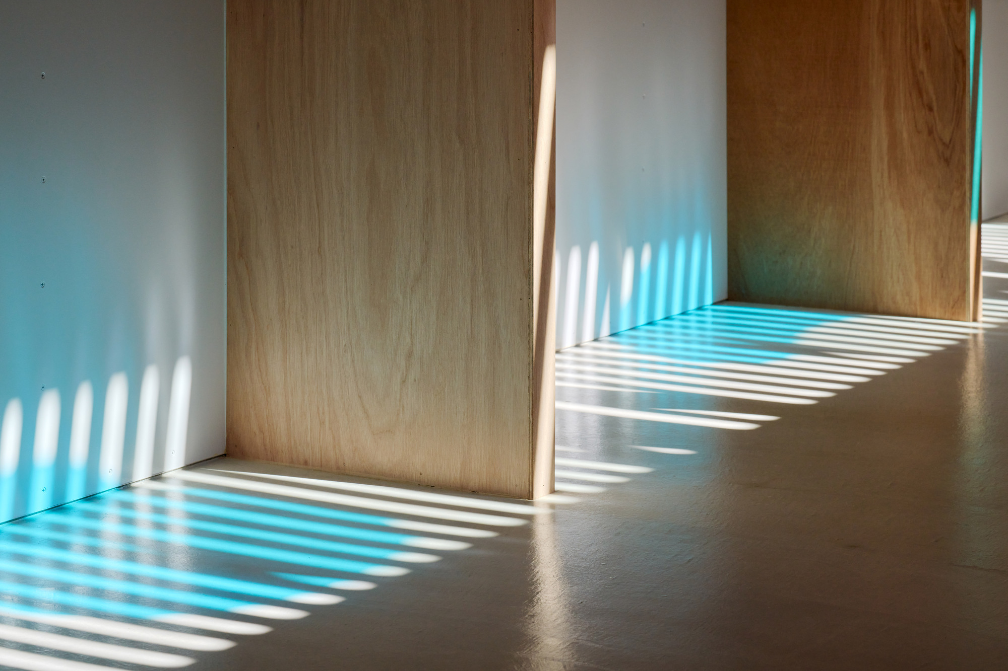 Light filtering through slatted screens casting striped patterns on white walls and plywood doors