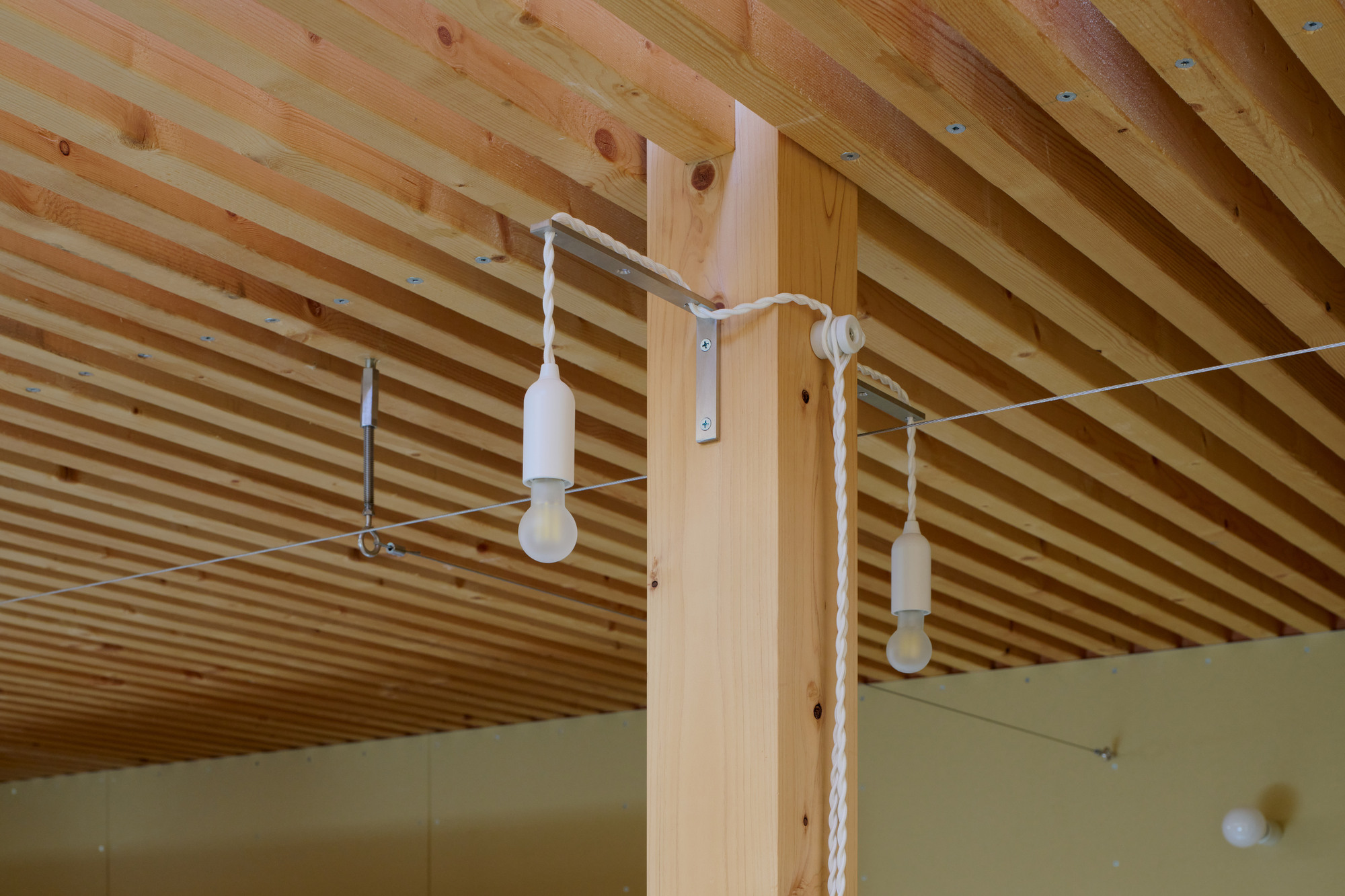 White cord pendant lights suspended from timber post beneath exposed slatted ceiling joists