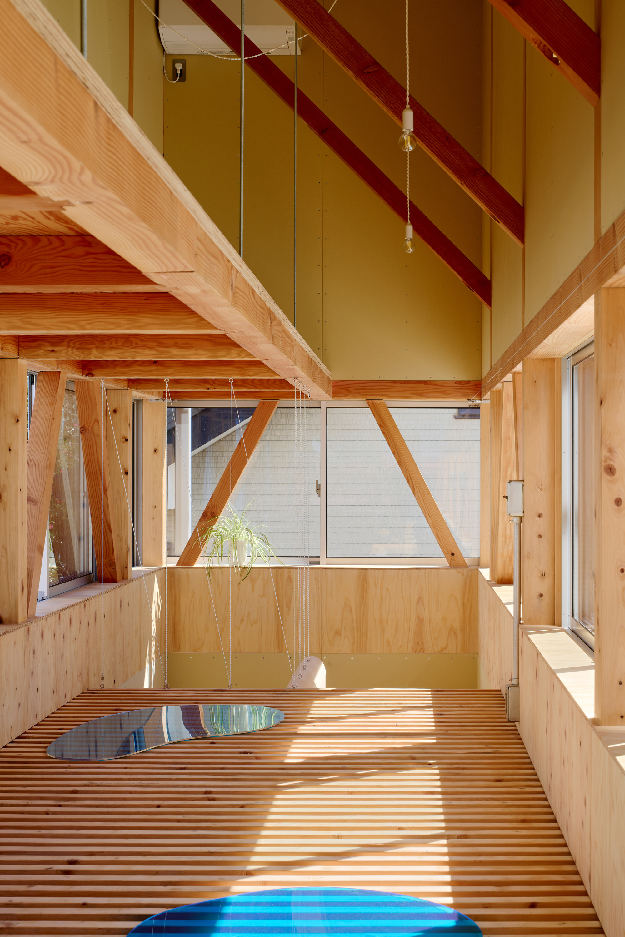 Interior view of slatted timber floor with diagonal structural beams crossing the vaulted ceiling in afternoon light
