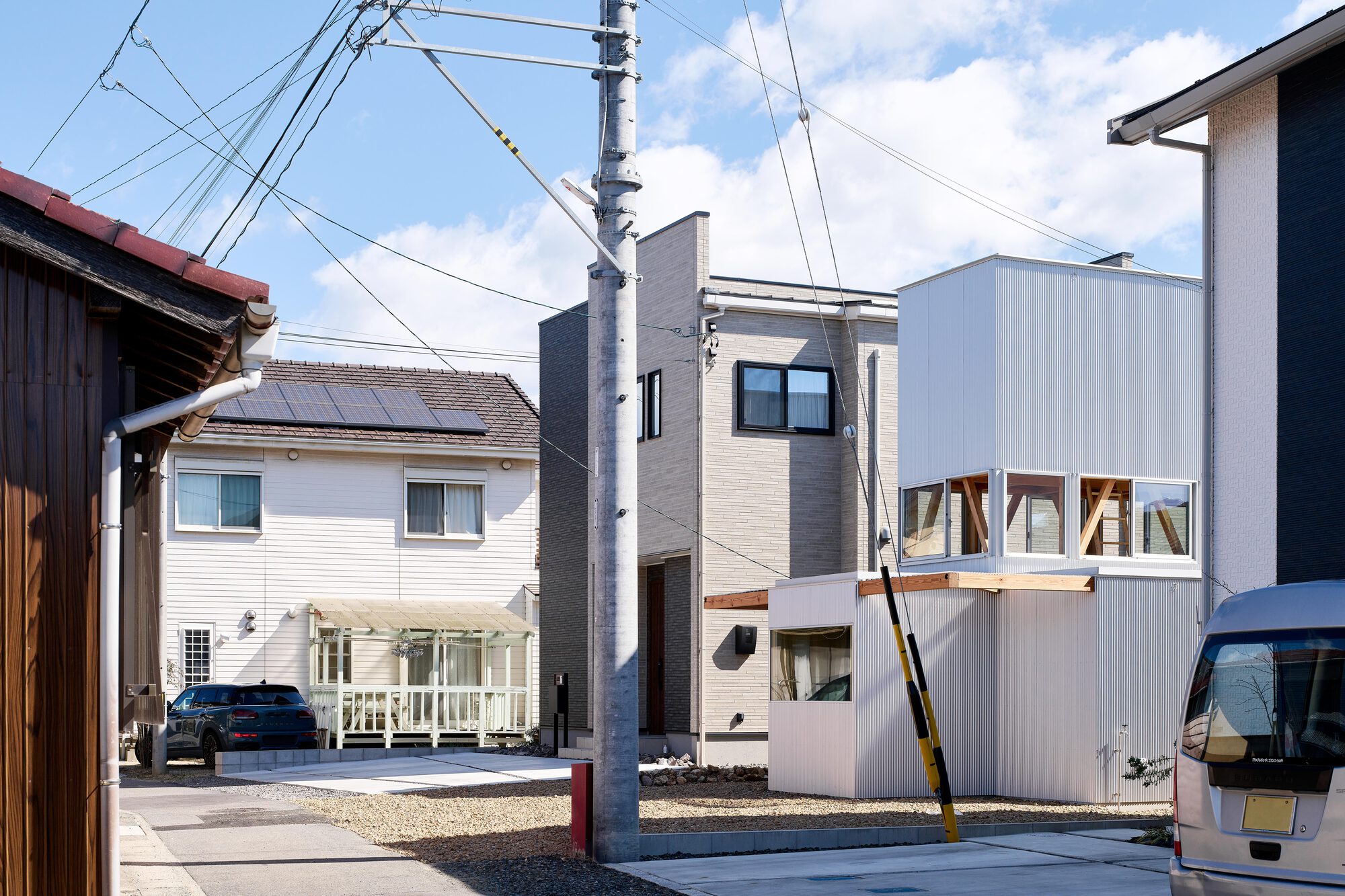 Street view showing corrugated metal volume with diagonal timber bracing beneath clerestory windows and overhead power lines